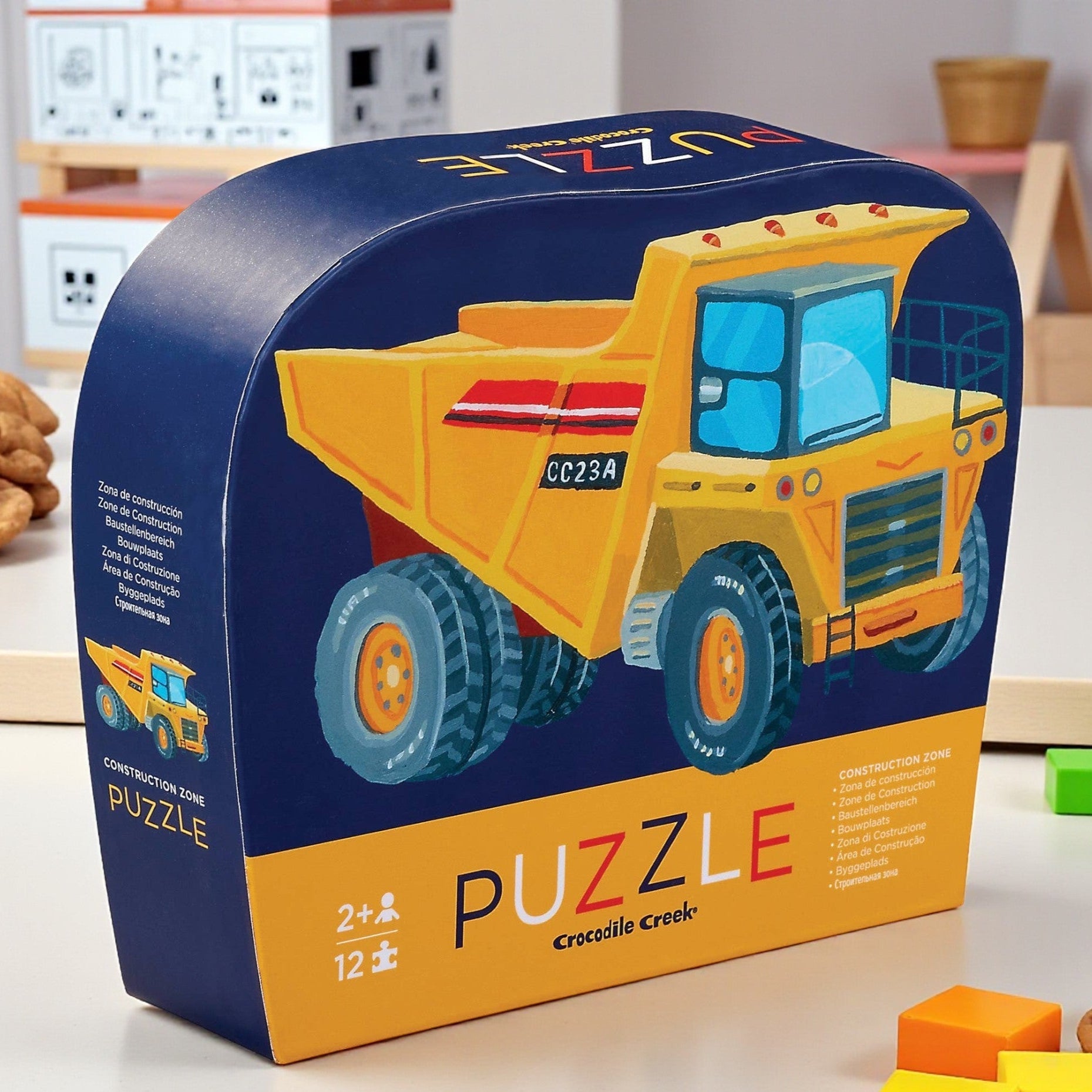 Boxed puzzle of a yellow dump truck with construction-themed elements on a table.