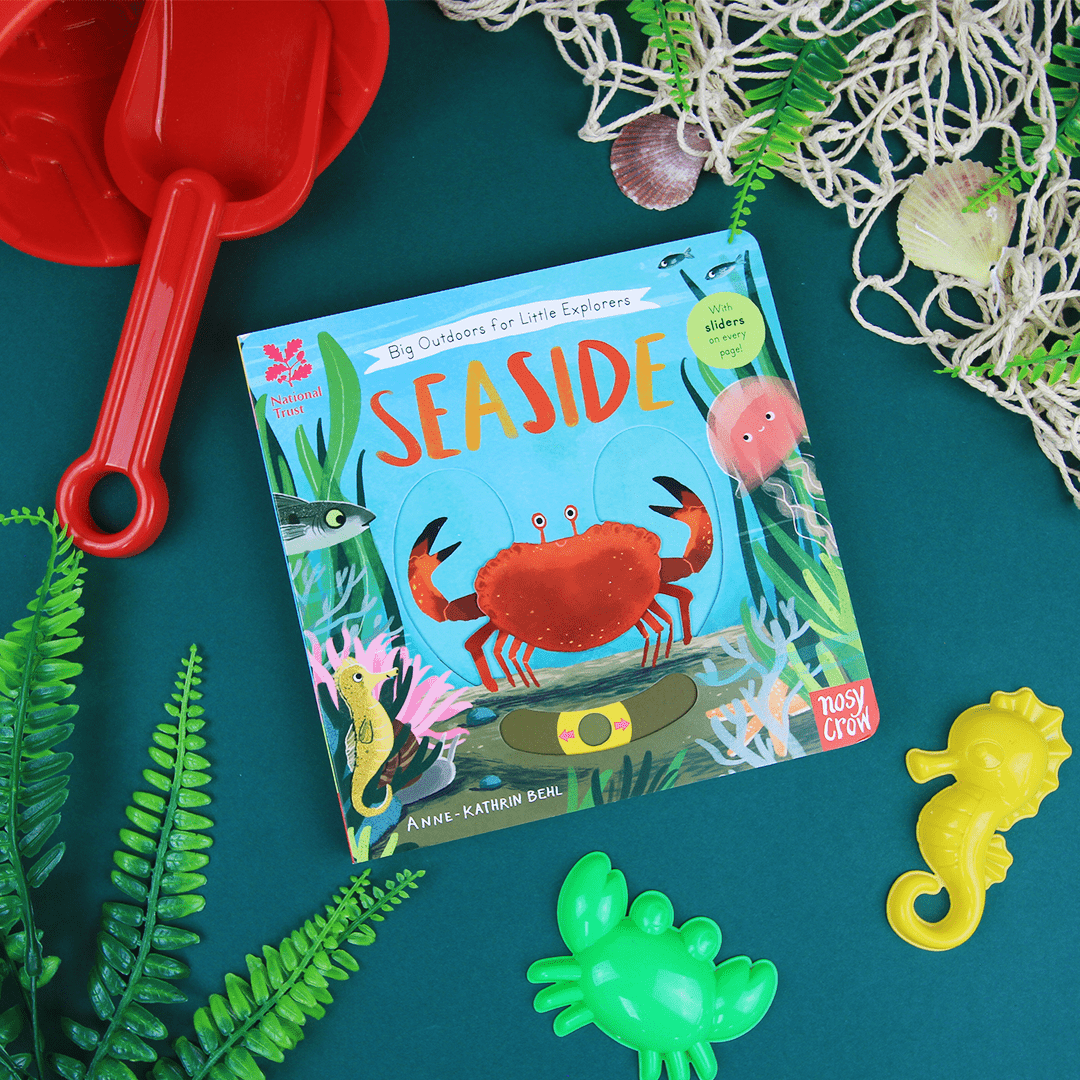 Children's book titled 'Seaside' surrounded by beach-themed toys on a teal surface