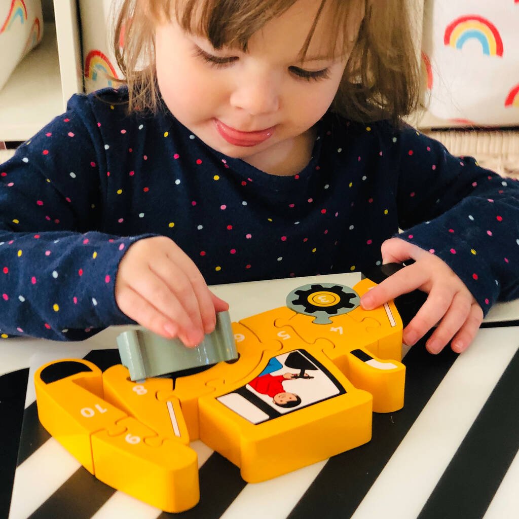 Child playing with a yellow tractor puzzle on a striped surface