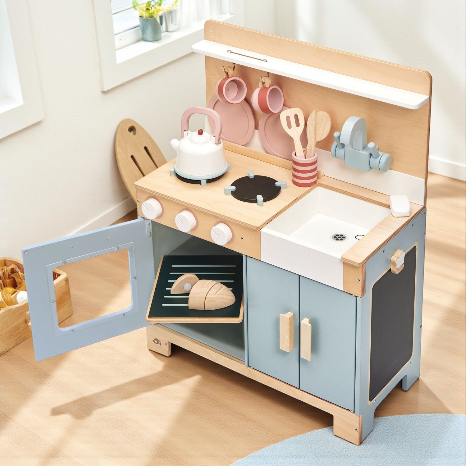 Wooden toy kitchen set with oven, stove, and sink on a light wooden floor.