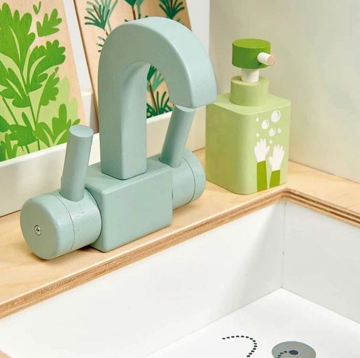 Children's toy faucet and soap dispenser set on a wooden surface with a floral-patterned wall in the background.