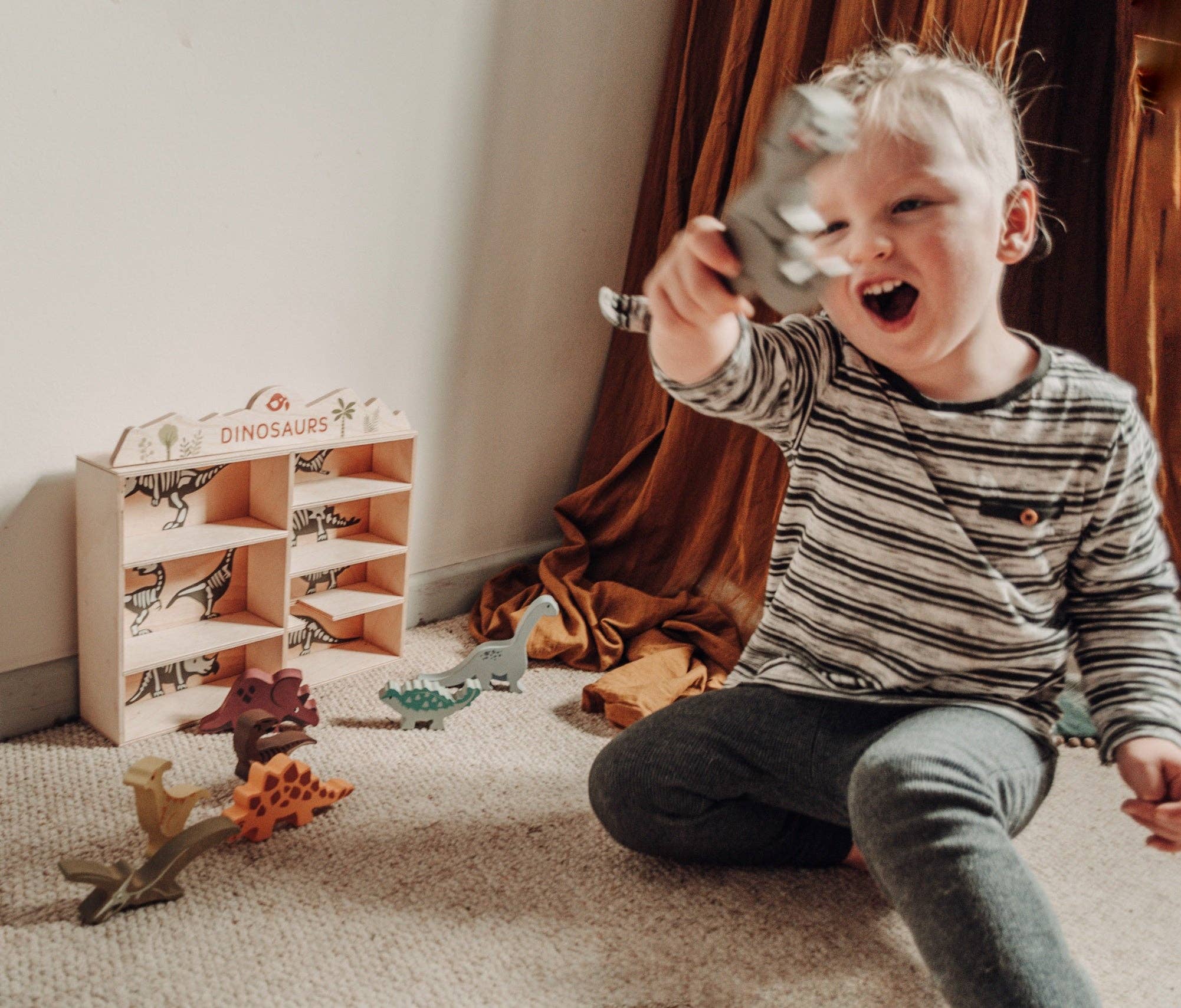 Child playing with dinosaur toys in a room with a dinosaur toy set.