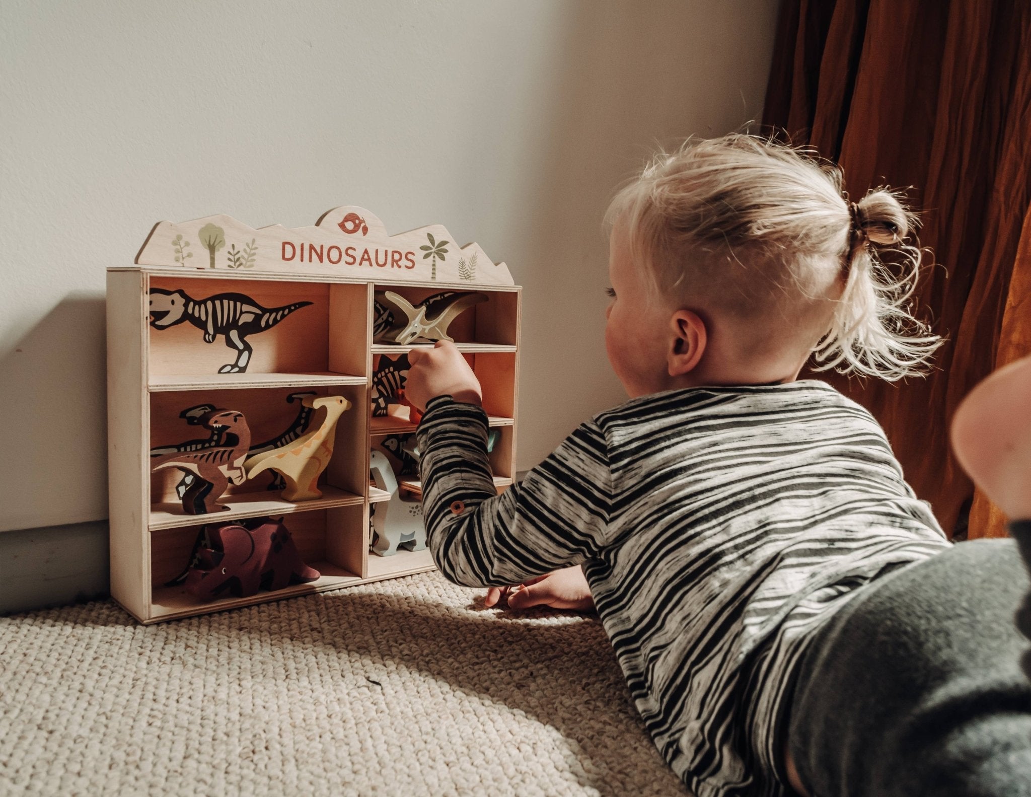 Child playing with a toy dinosaur set in a wooden box labeled 'Dinosaurs'.