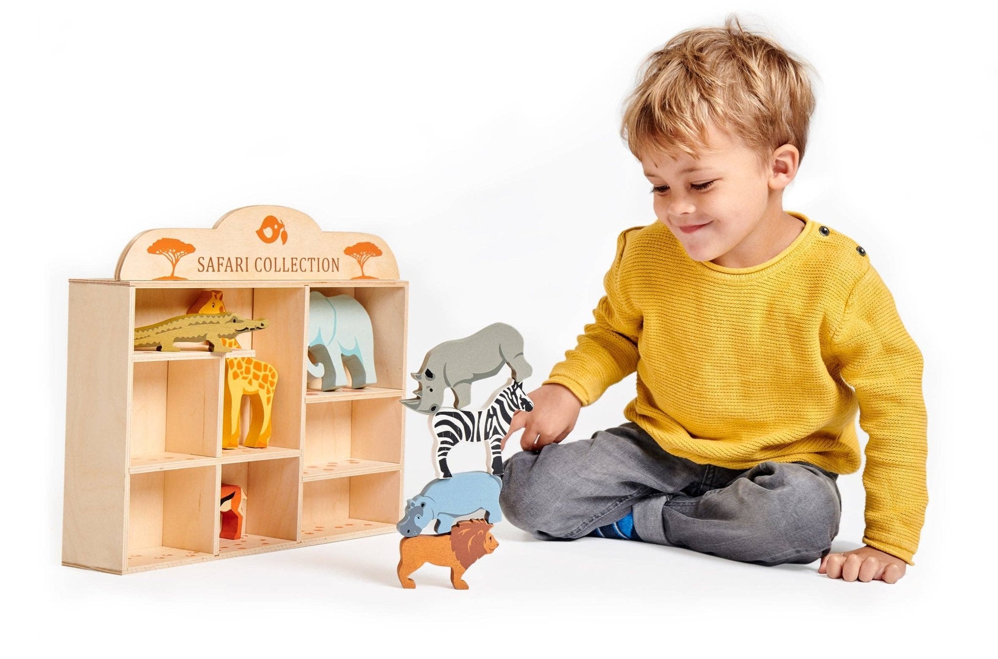 Child playing with toy animals in front of a wooden toy shelf labeled 'Safari Collection'.