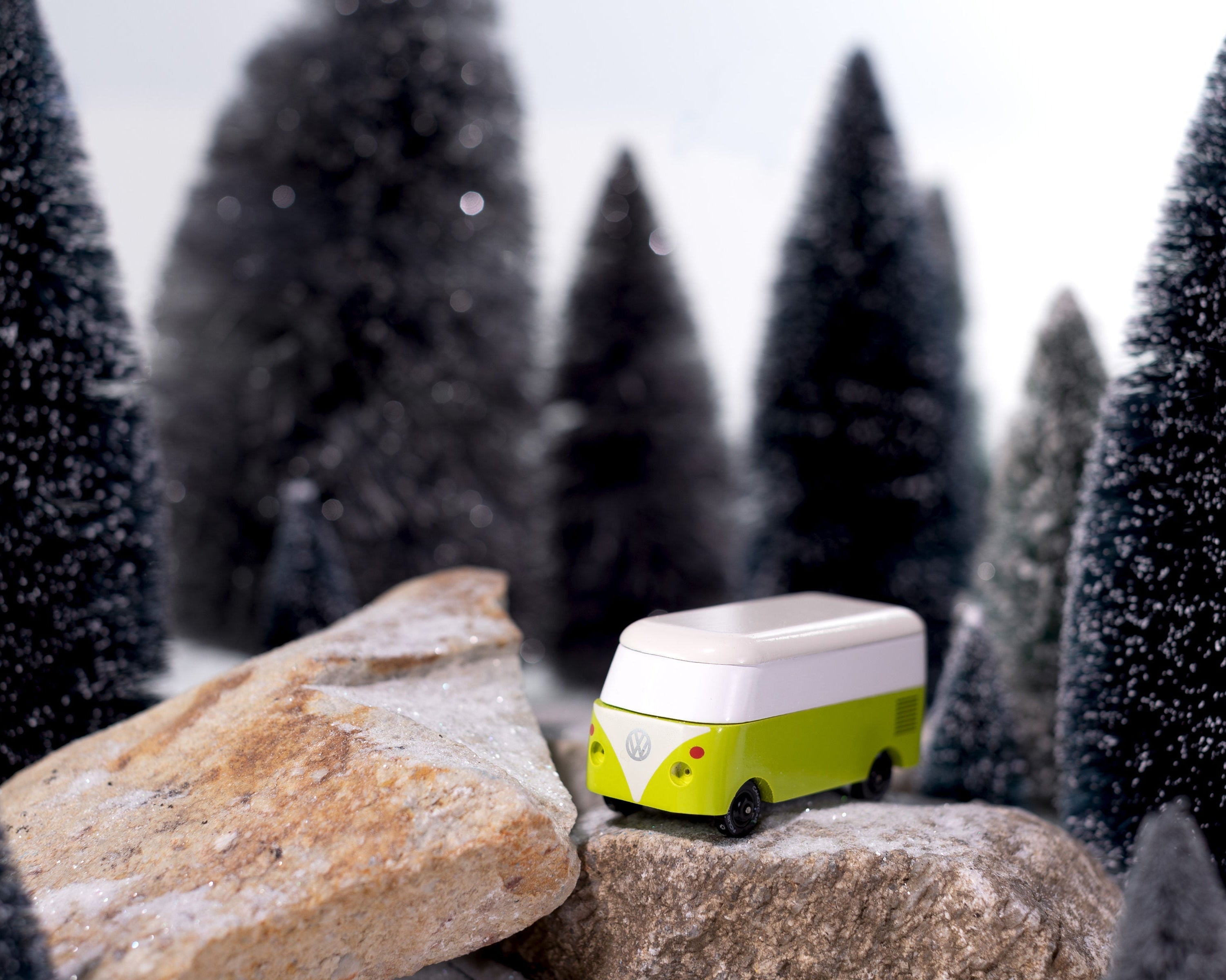 Small green and white vehicle on a rock with snowy trees in the background