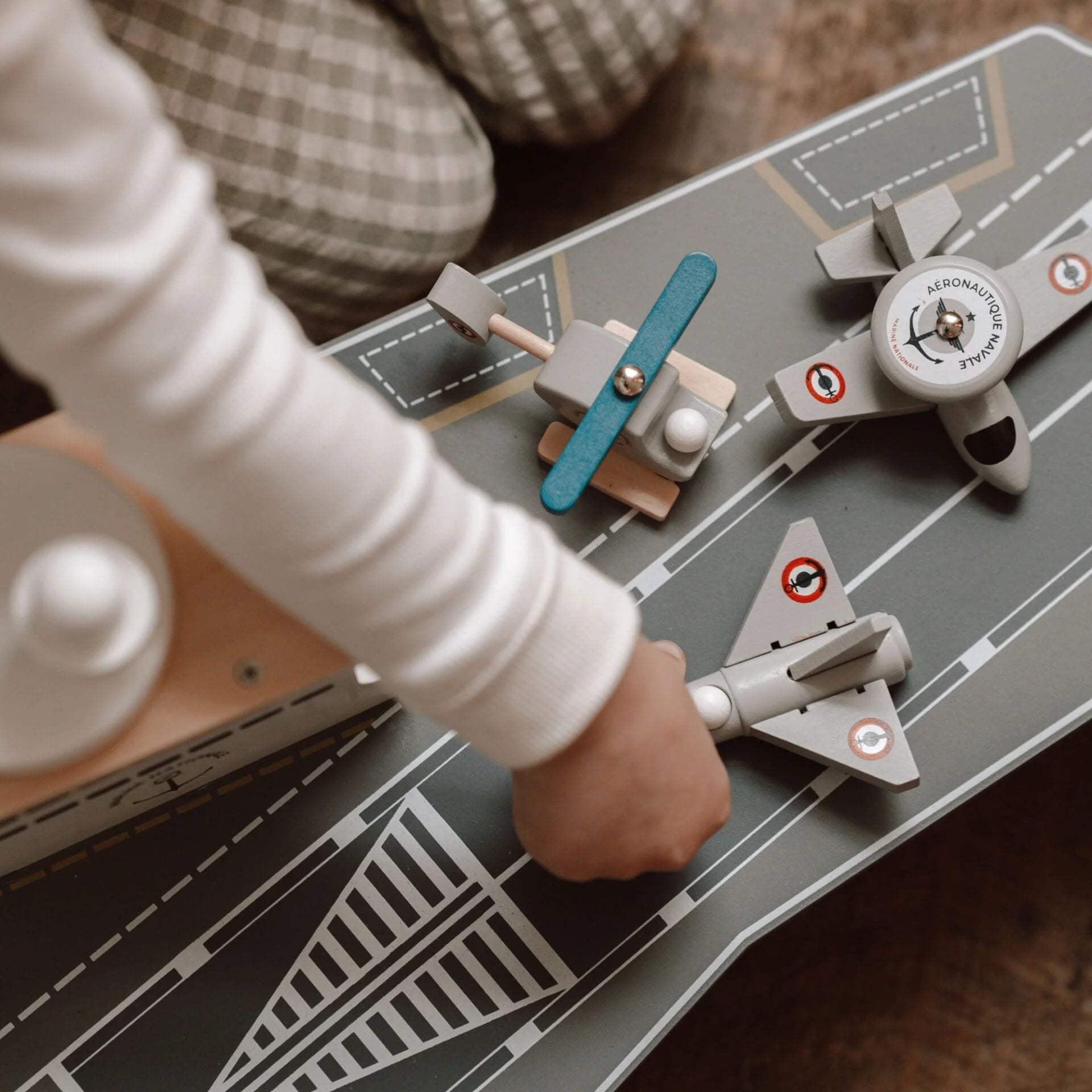 Child playing with a toy airplane on a play mat with roads and buildings.