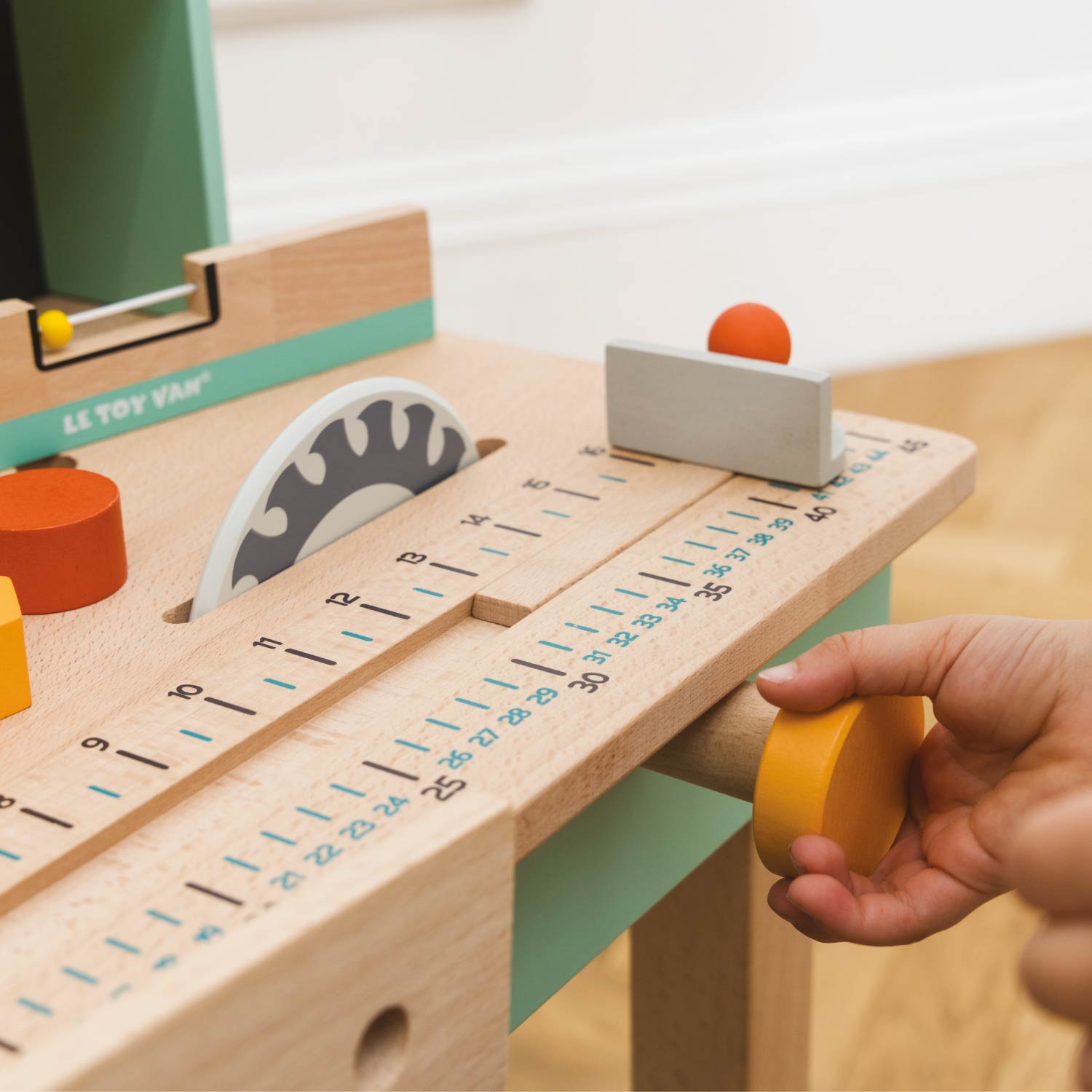 Wooden toy construction set with a hand holding a yellow wheel, featuring Le Toy Van branding.