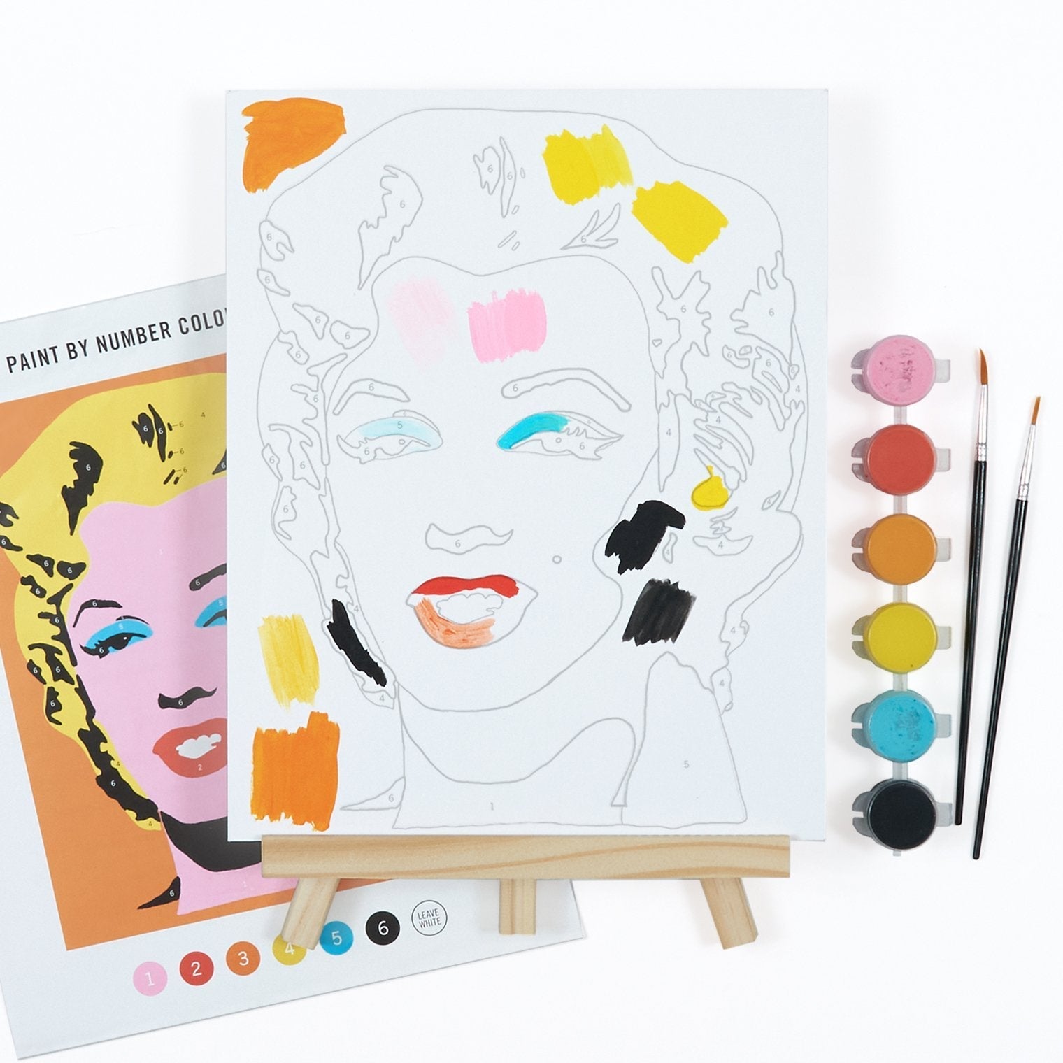 Coloring book with a face design, paintbrushes, and paint bottles on a white background