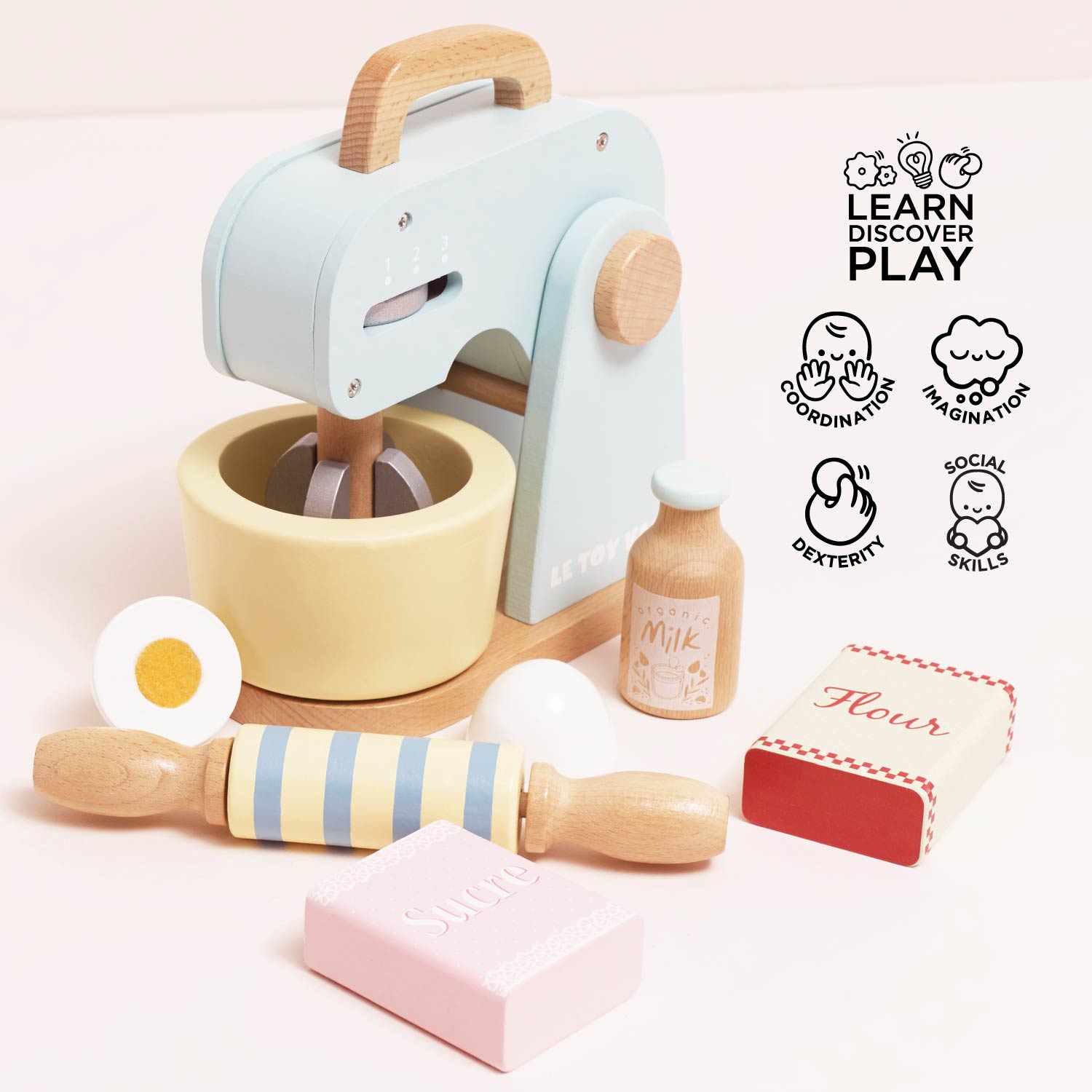 Children's toy kitchen set with mixer, rolling pin, and ingredients on a light pink background.