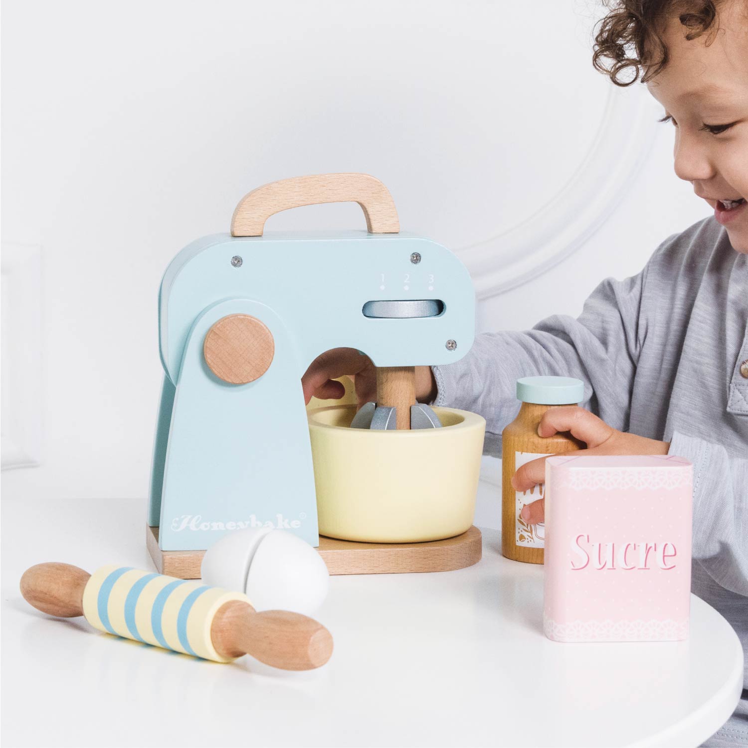 Child playing with a toy kitchen set on a white surface
