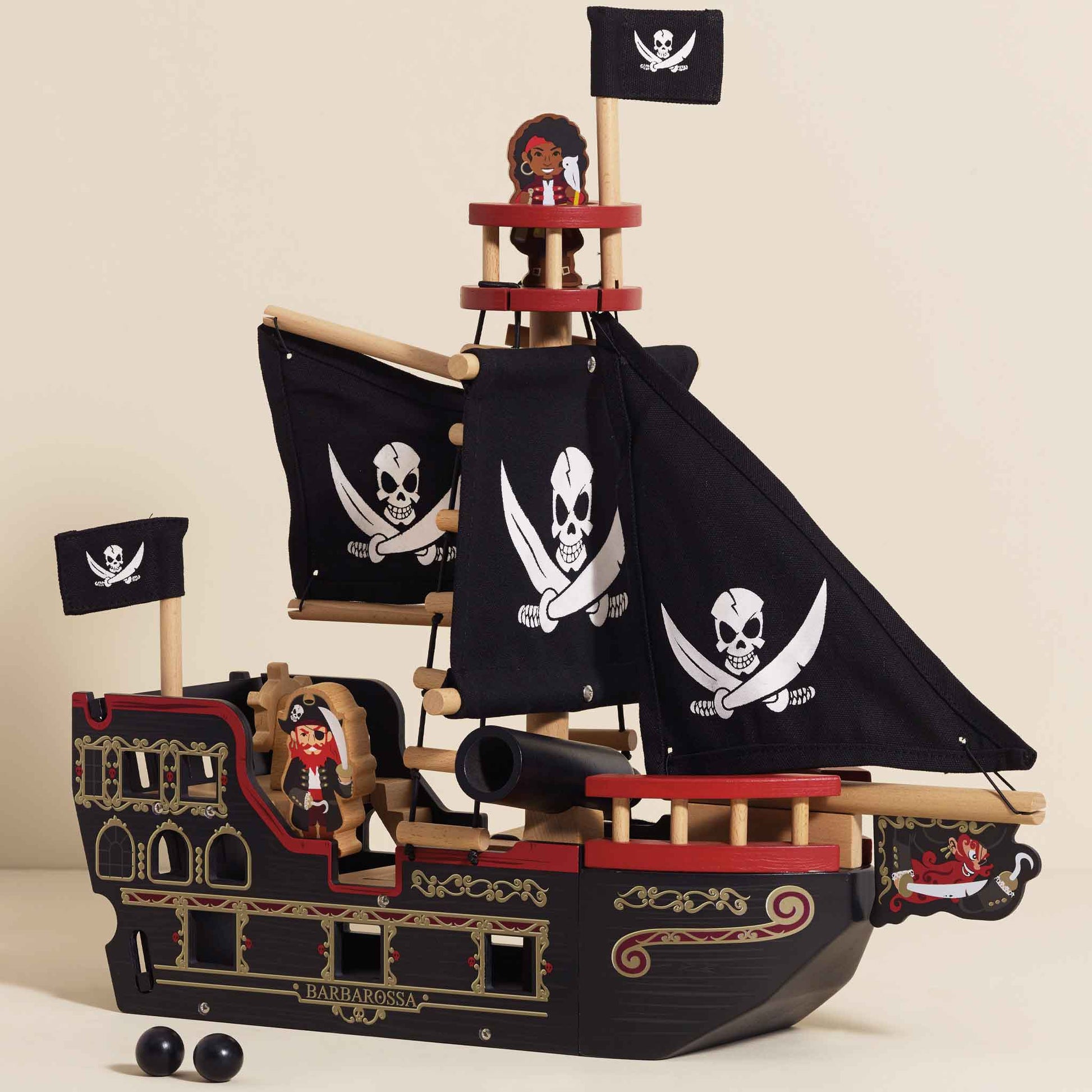Wooden toy pirate ship with black sails and flags on a beige background