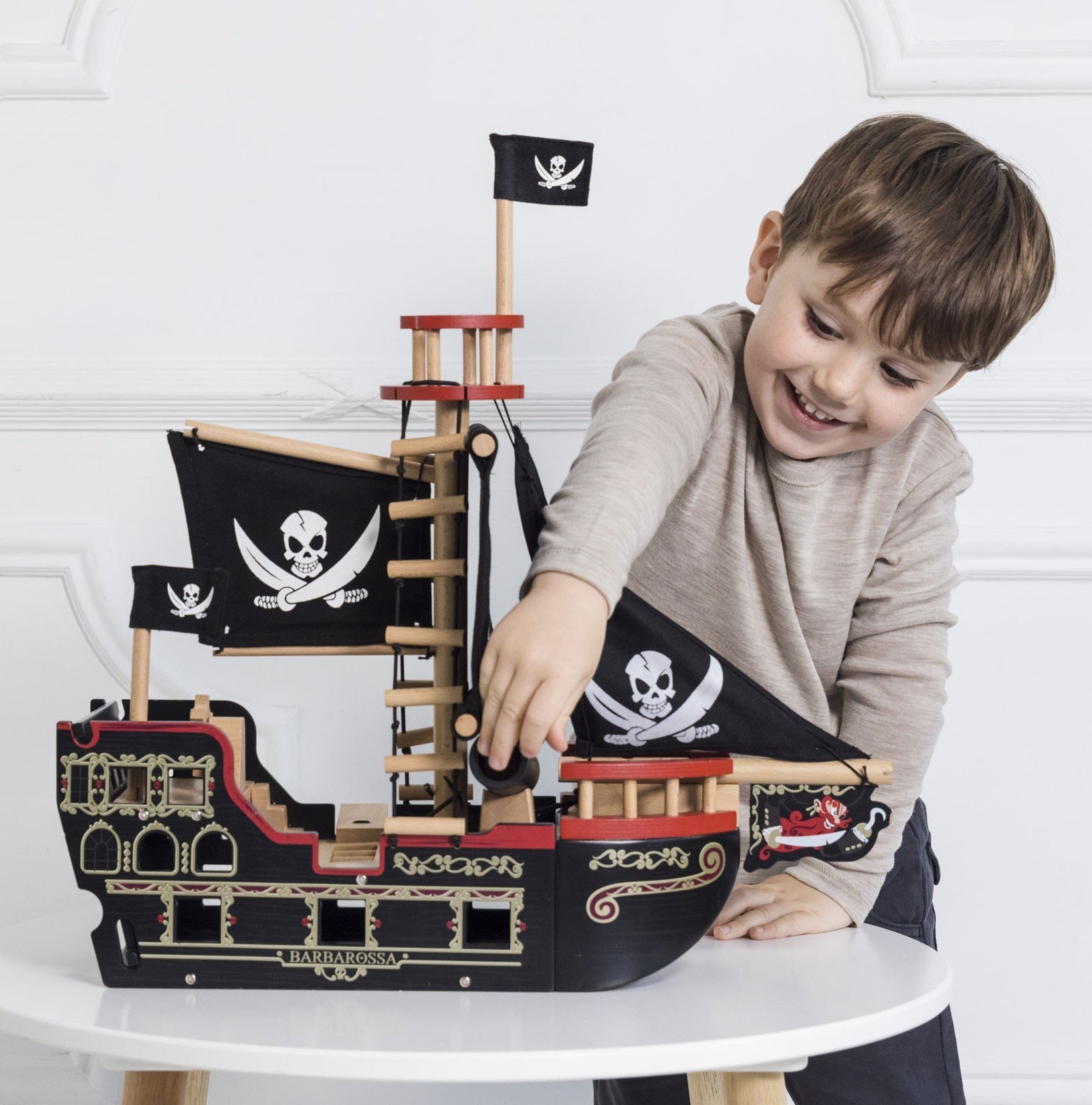 Child playing with a wooden pirate ship toy on a white surface.