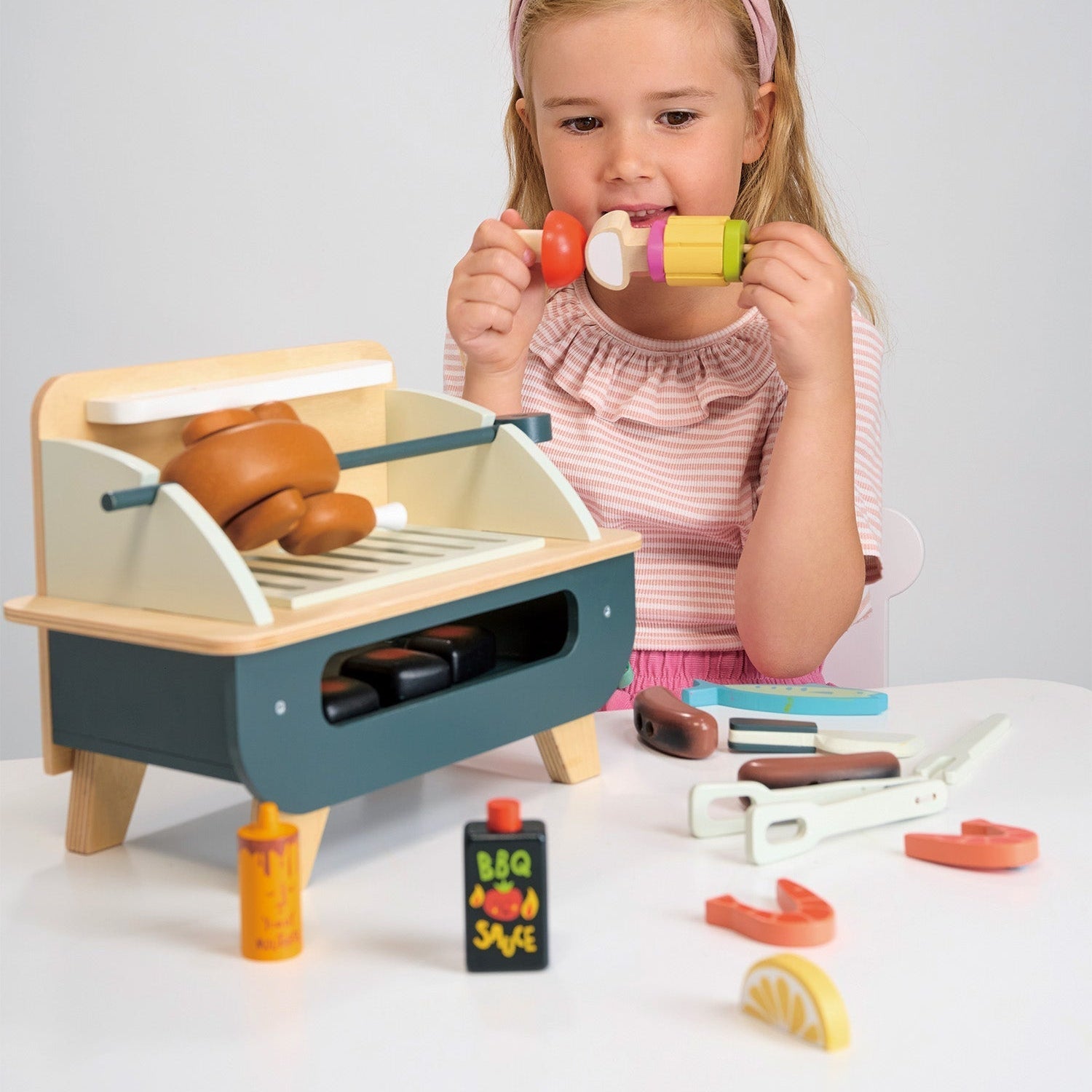 Child playing with a toy grill set on a white surface