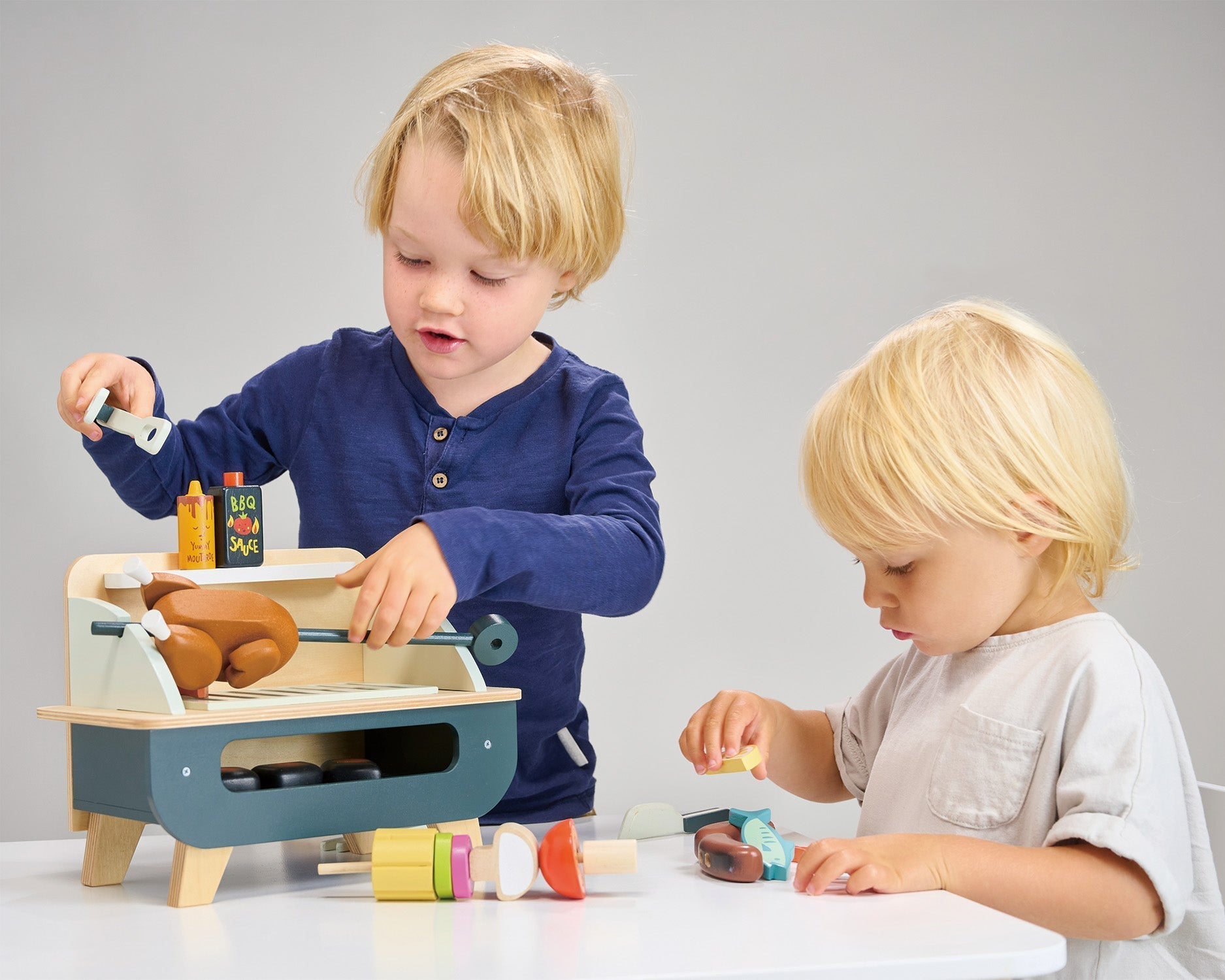 Two children playing with a wooden toy set on a gray background