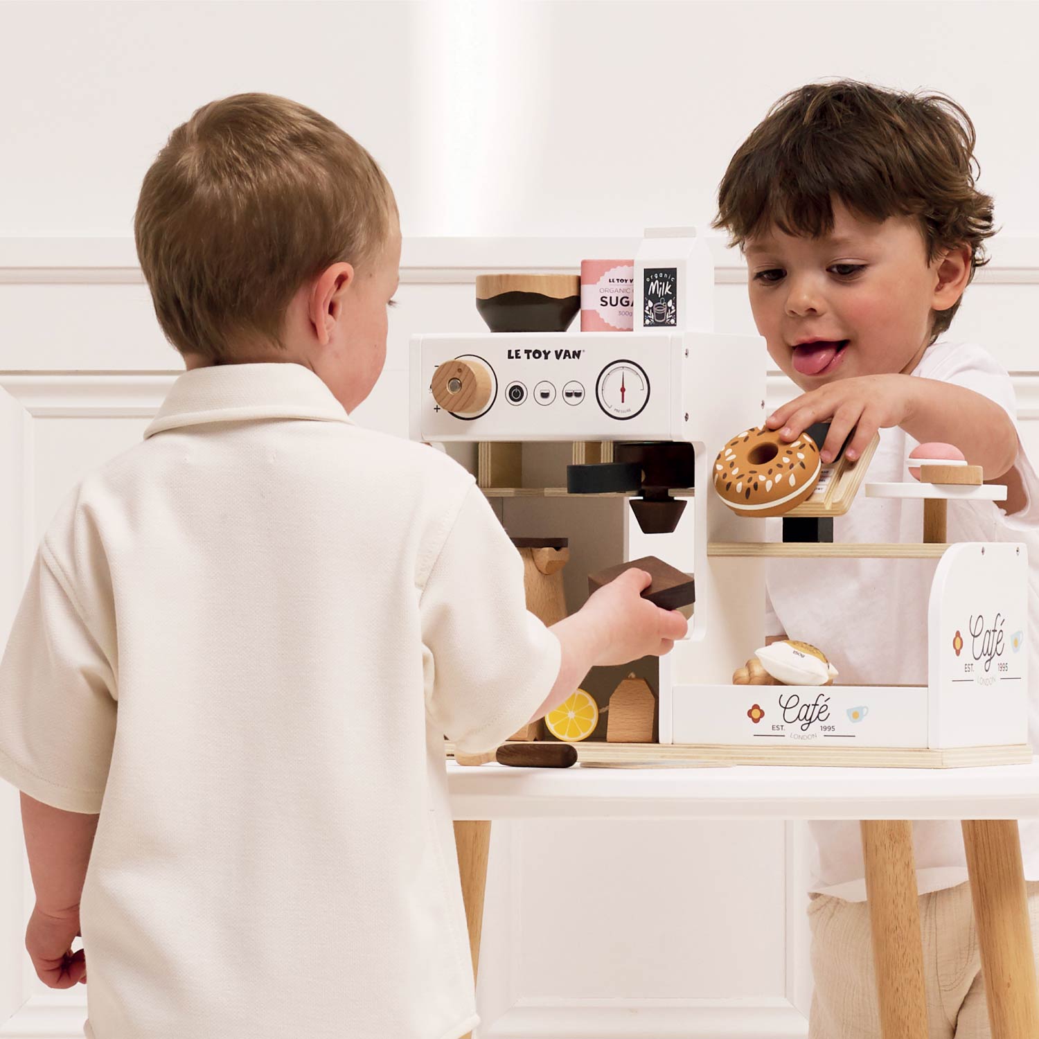 Two children playing with a toy coffee shop set on a white background