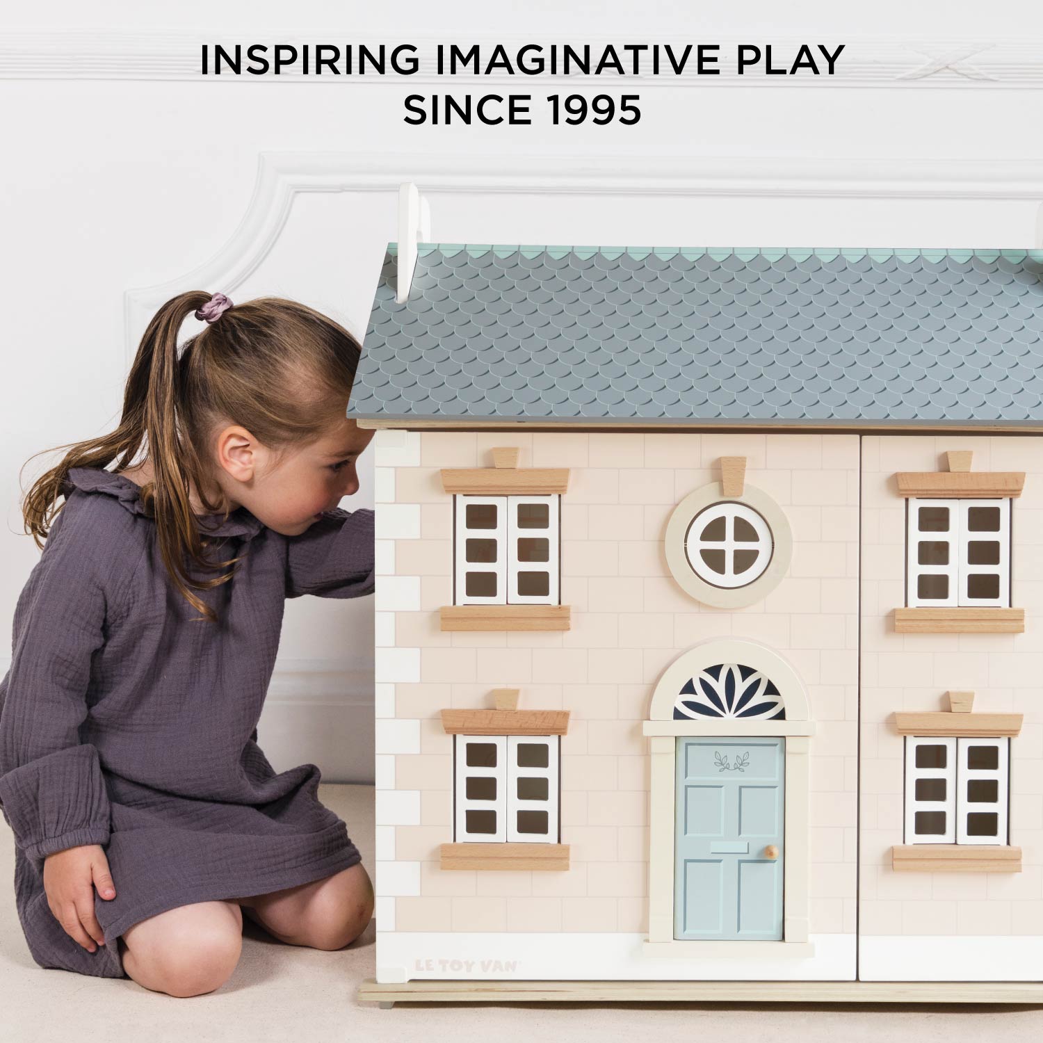 Child playing with a wooden dollhouse, with text 'Inspiring Imaginative Play Since 1995'.