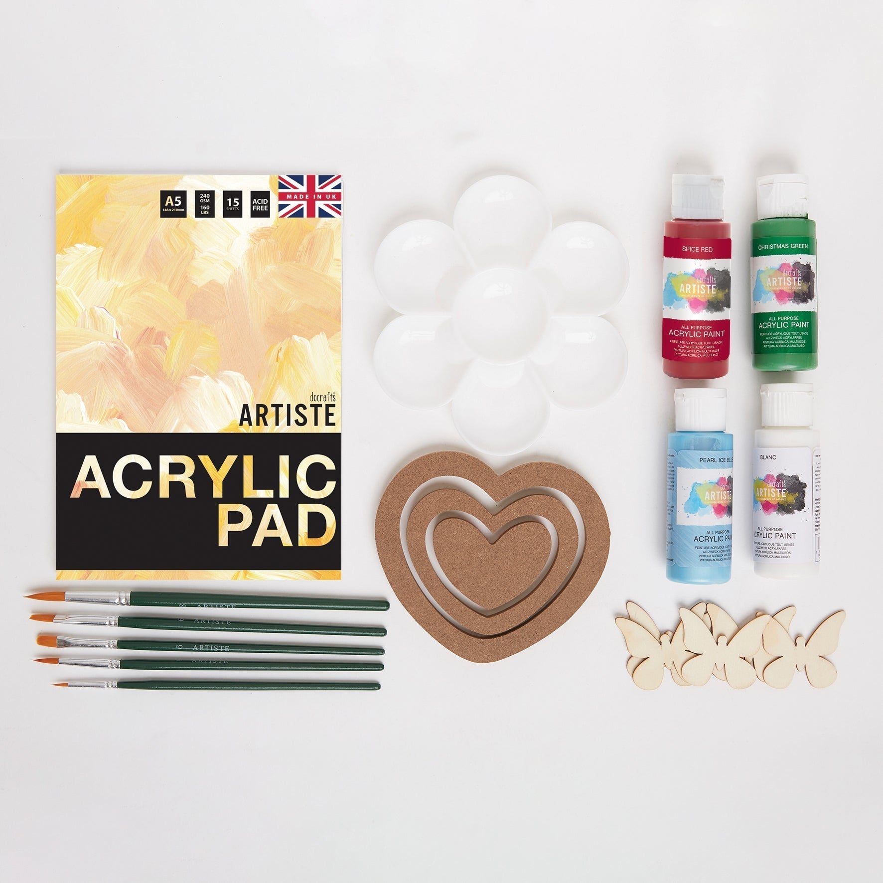 Art supplies including an acrylic pad, paint bottles, brushes, and wooden shapes on a white background