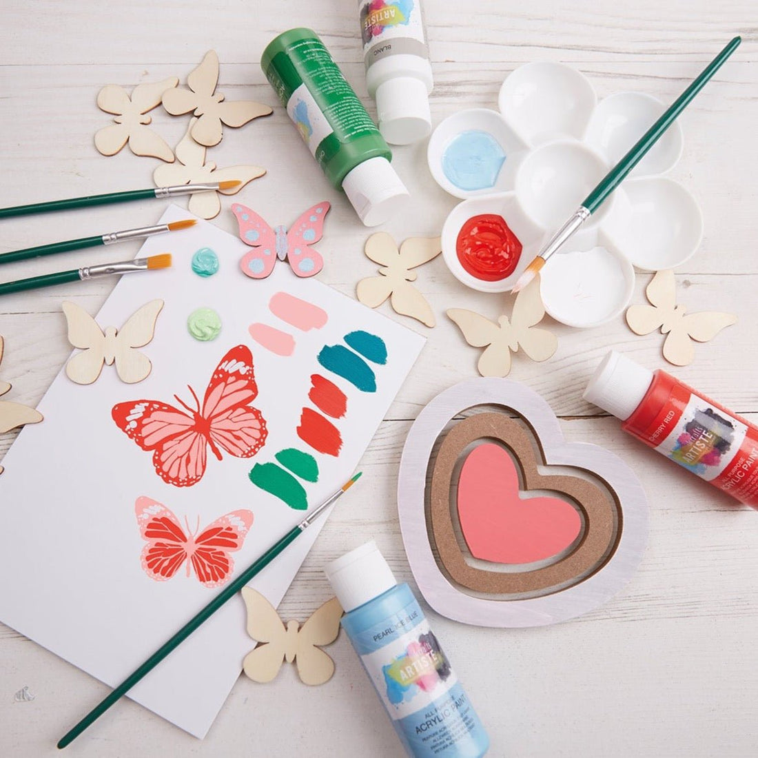 Art supplies including paint, brushes, and decorative items on a wooden surface