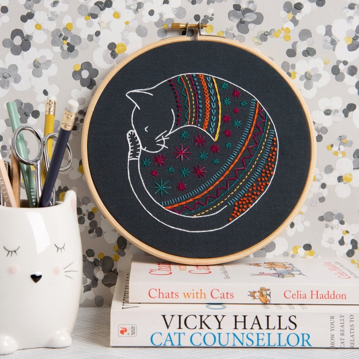 Embroidery hoop with a colorful cat design on a book and stationery items.