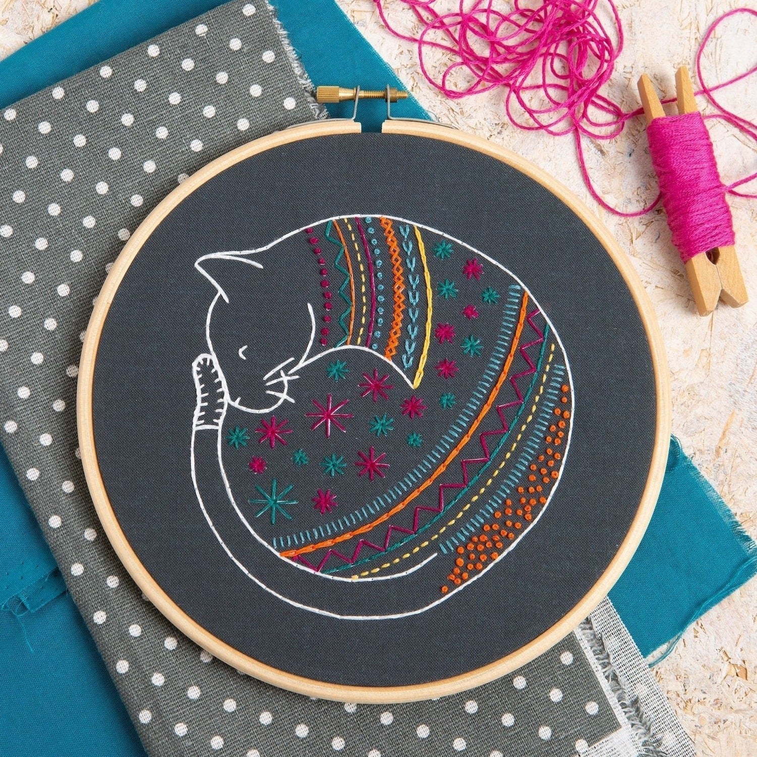 Embroidery hoop with a colorful cat design on a polka dot fabric background.