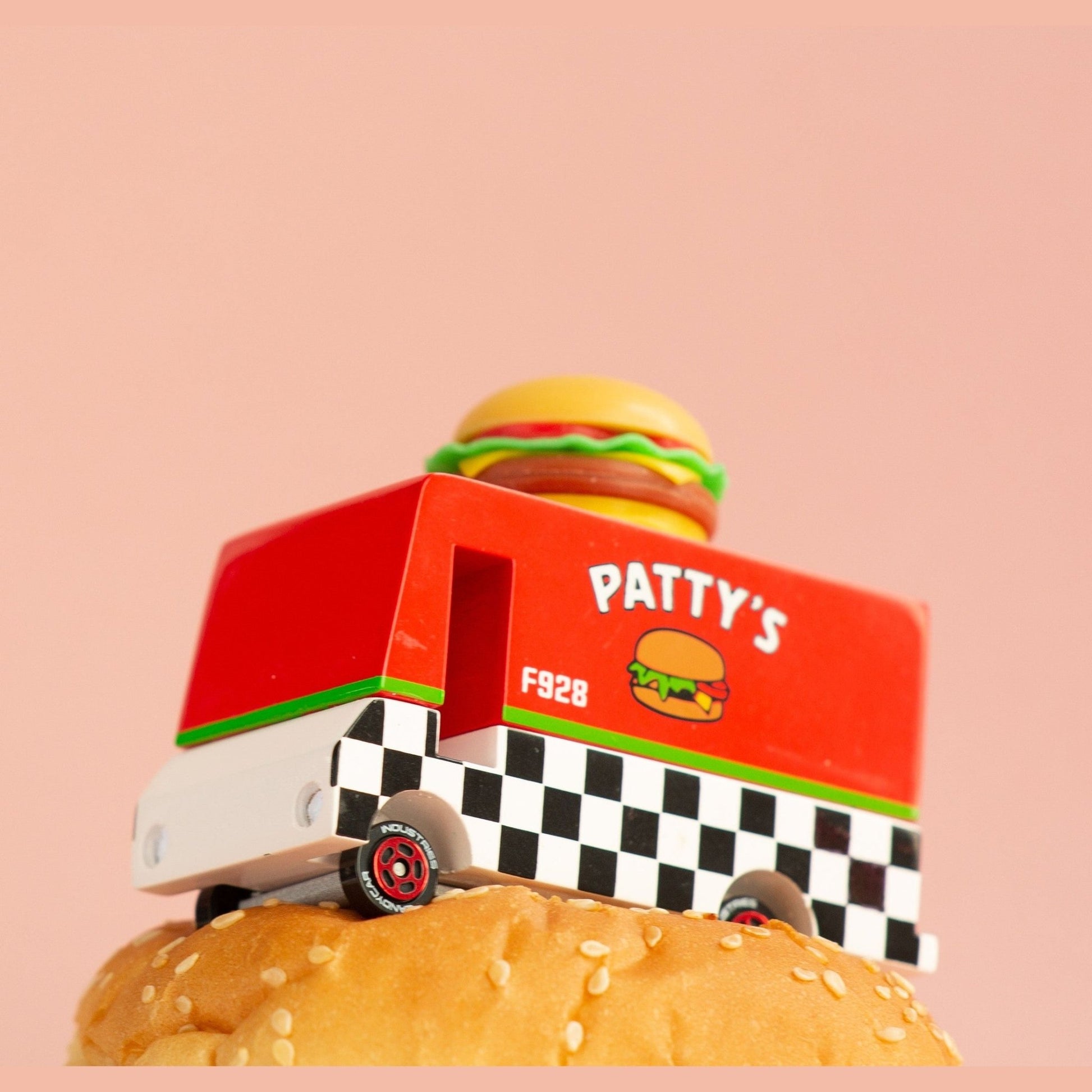 Toy truck with a hamburger on top of a burger against a pink background