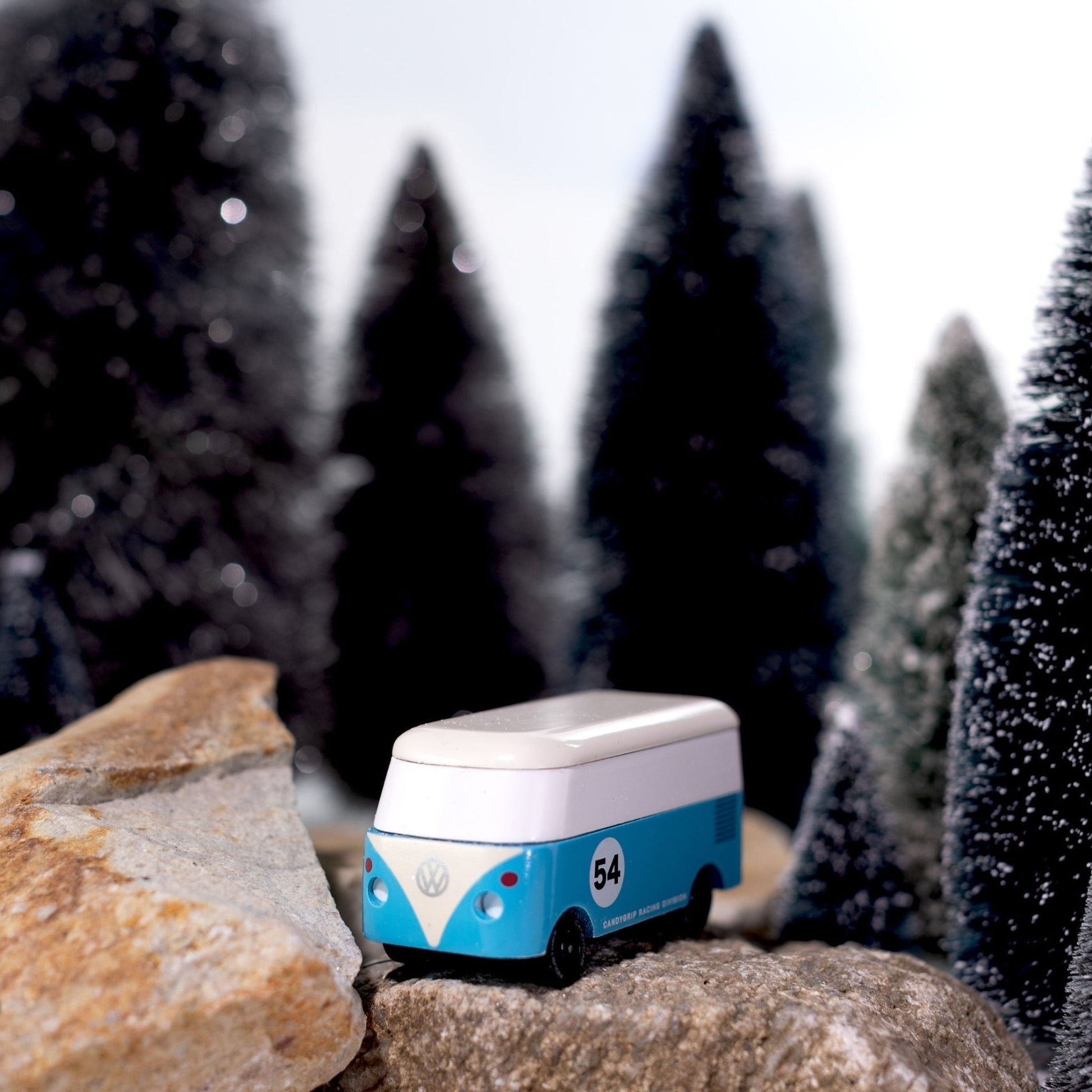 Model of a blue and white van on rocks with a snowy forest background