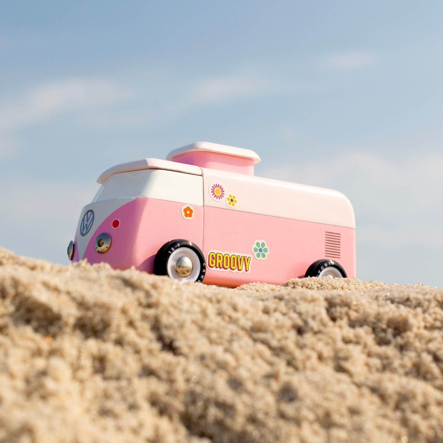 Pink and white vintage-style camper van on a sandy beach with a clear blue sky.