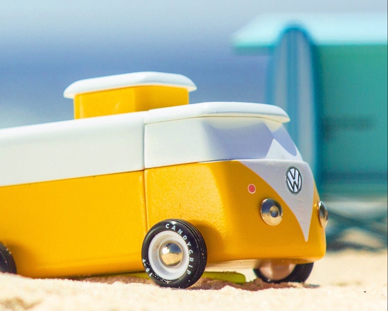 Yellow and white toy van on a sandy beach with ocean in the background