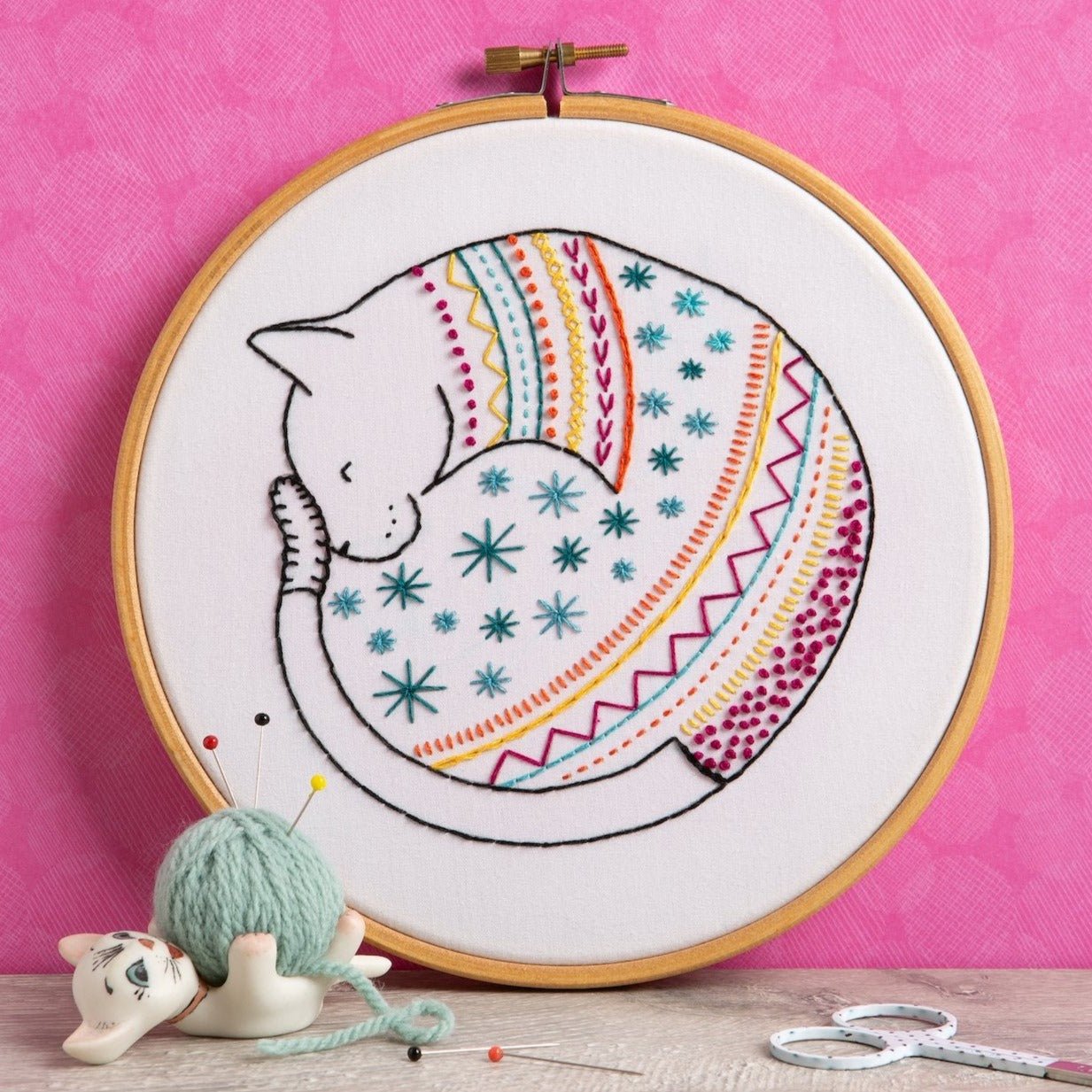 Embroidery hoop with a cat and rainbow design on a pink background