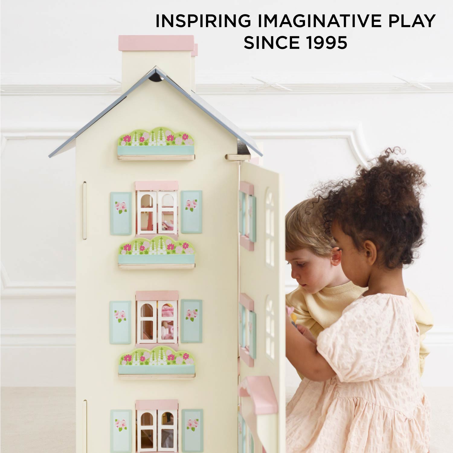 Children playing with a toy dollhouse, inspired by imaginative play since 1995.