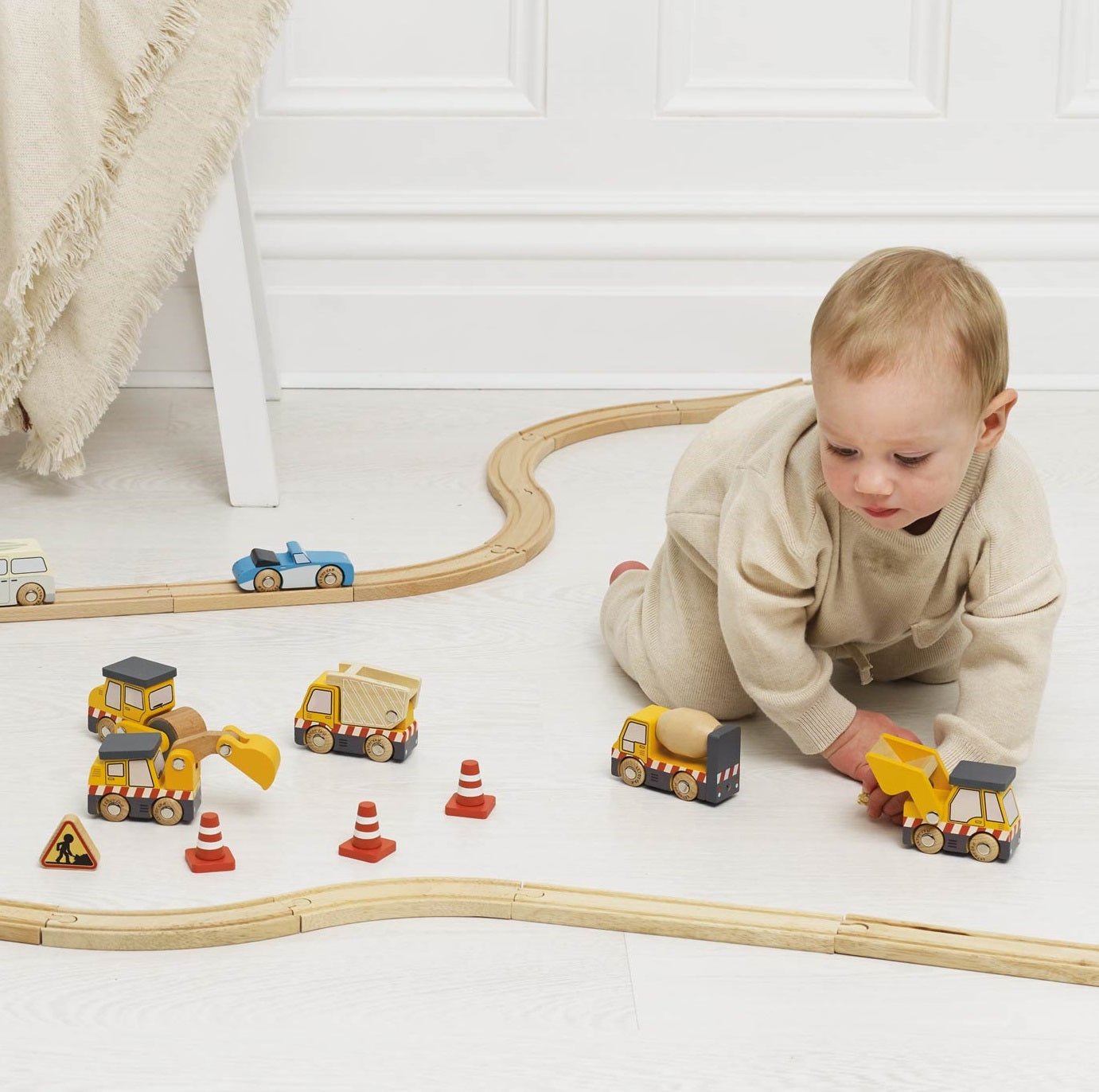 Child playing with toy cars and tracks on a white floor.