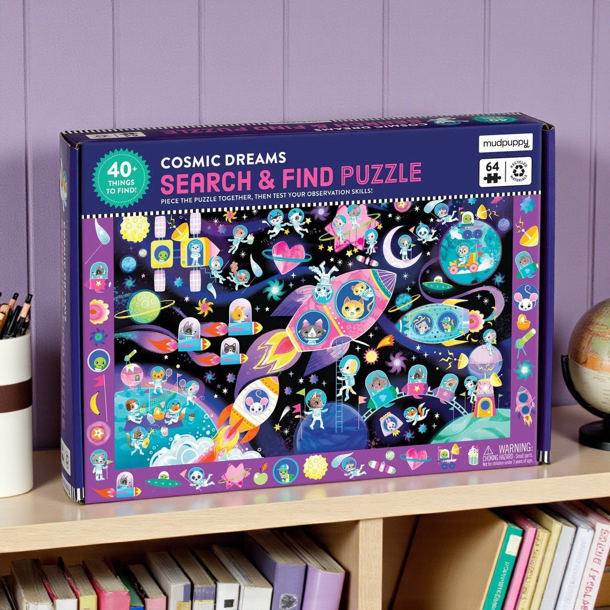 Cosmic Dreams Search & Find Puzzle box on a shelf with books and a globe.
