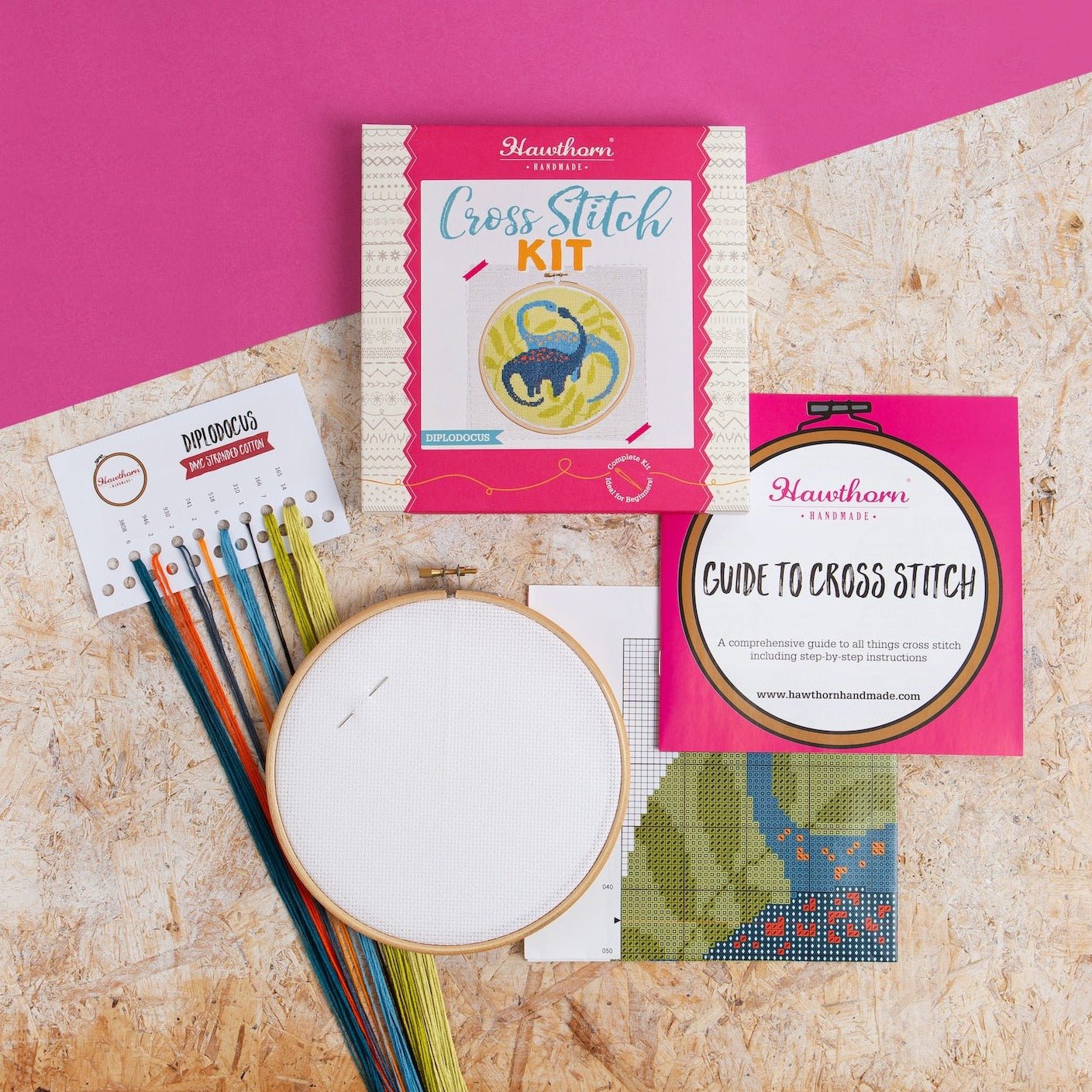 Cross stitch kit with materials on a textured surface and pink background