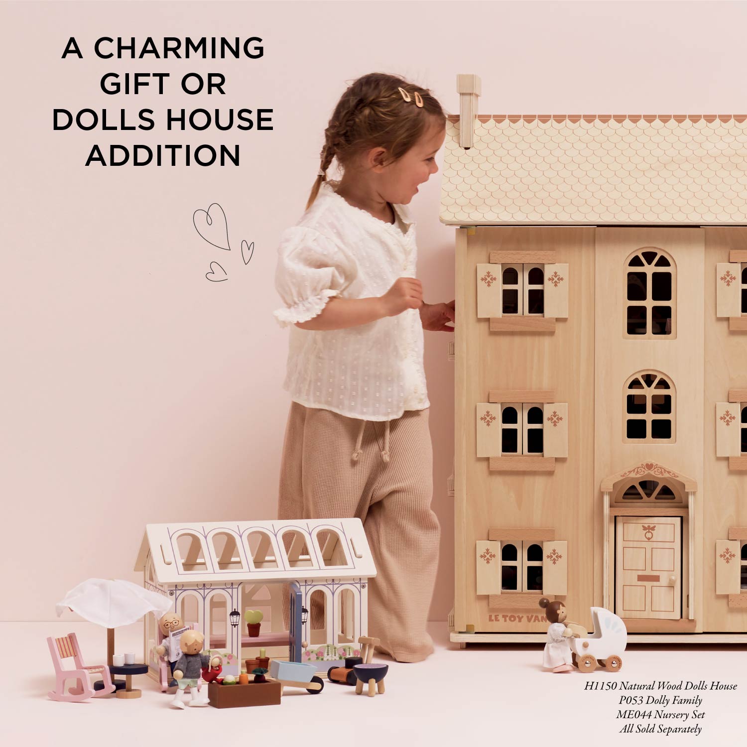 Child playing with a wooden dolls' house and accessories on a light pink background