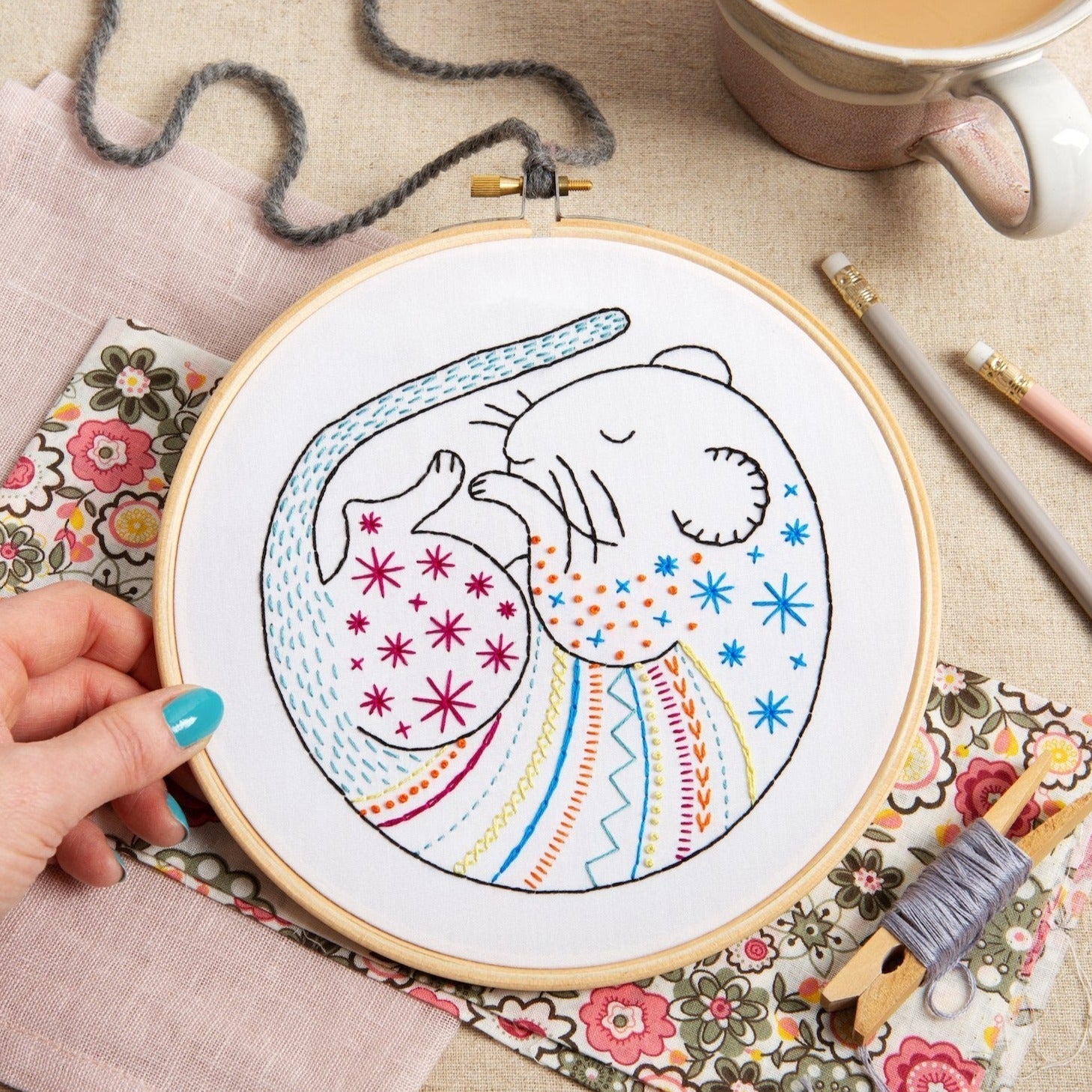 Embroidery hoop with a colorful design of a cat and star pattern on a floral fabric background.