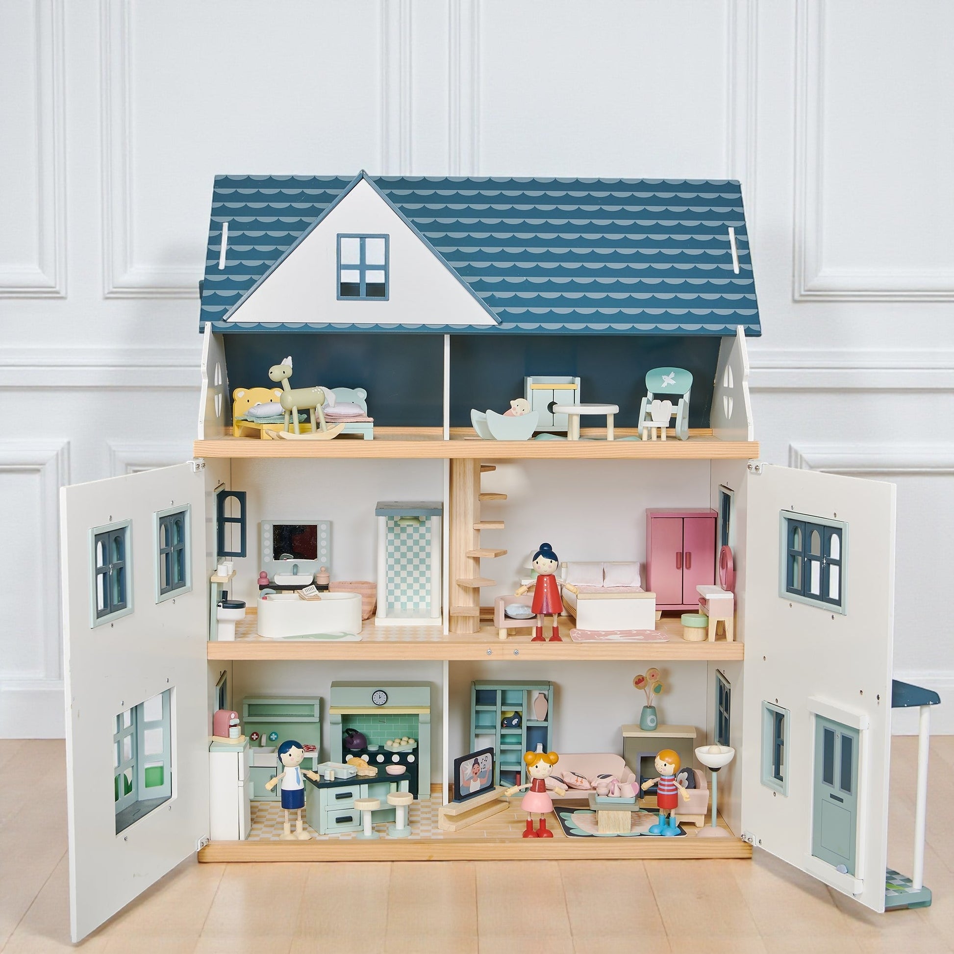 Wooden dollhouse with multiple rooms and furniture on a light wooden floor.