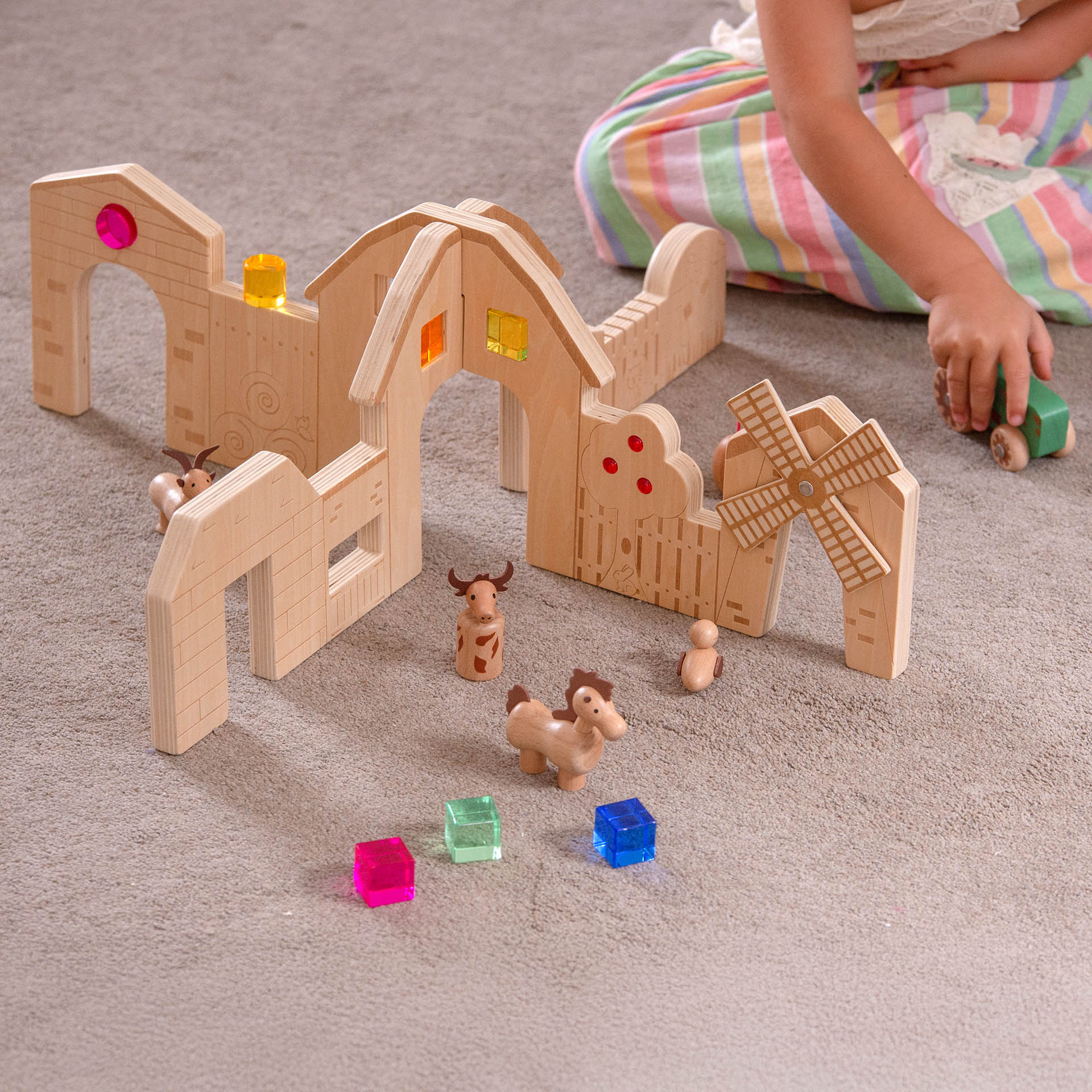 Wooden farm toy set with animals and buildings on a carpeted floor.