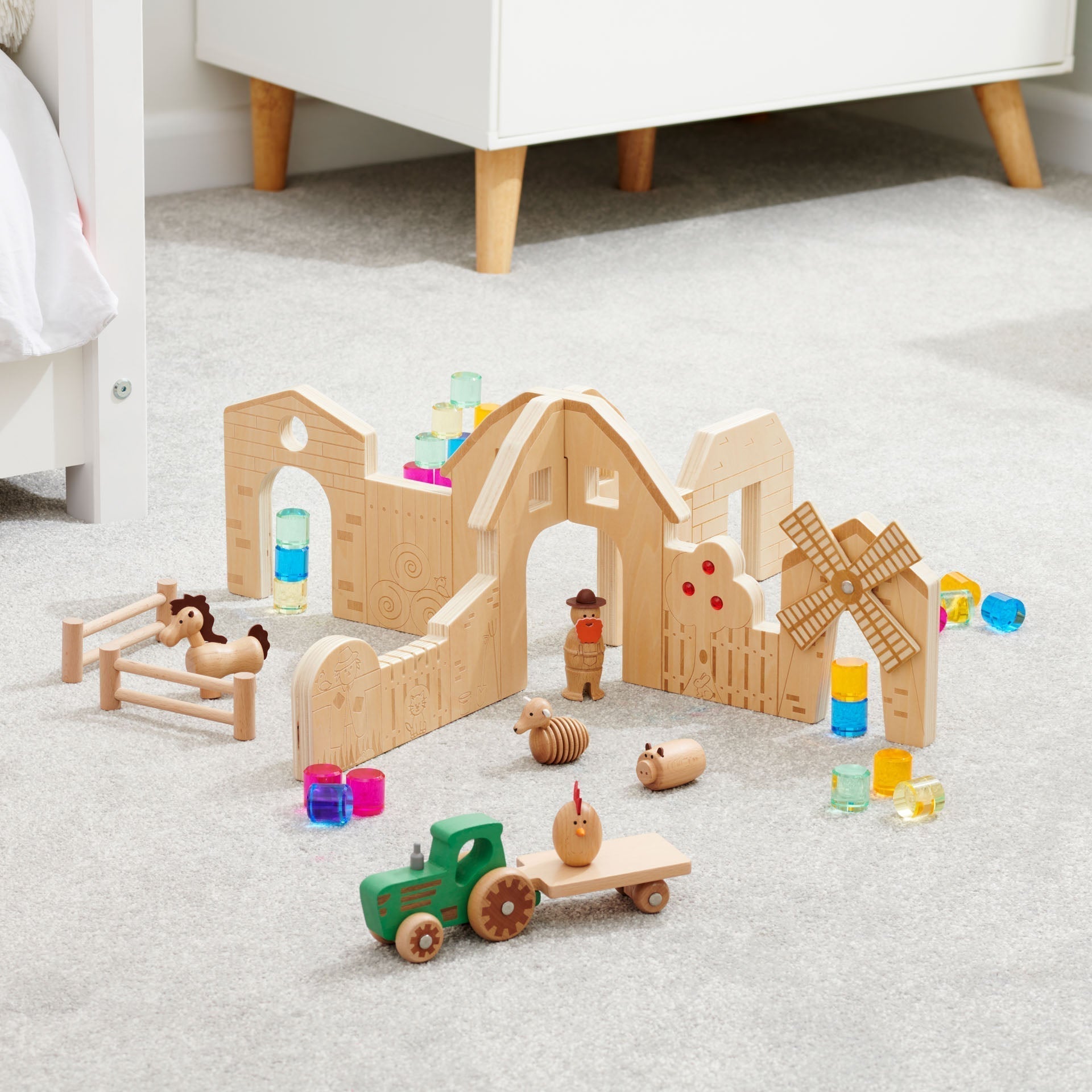 Wooden toy set with buildings, animals, and a tractor on a carpeted floor.