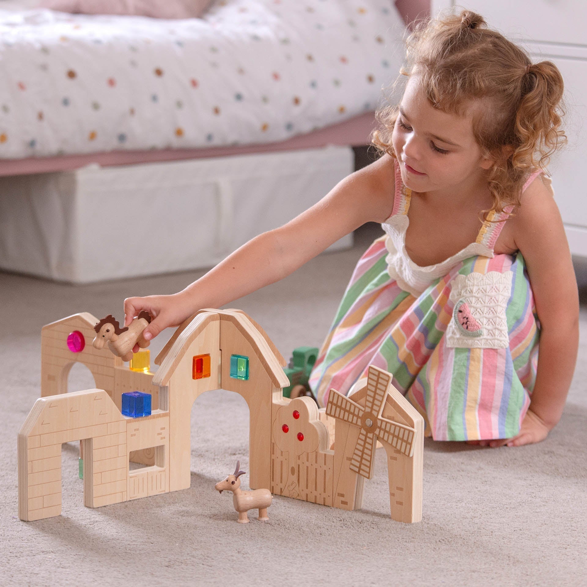Child playing with a wooden farm toy set on the floor.