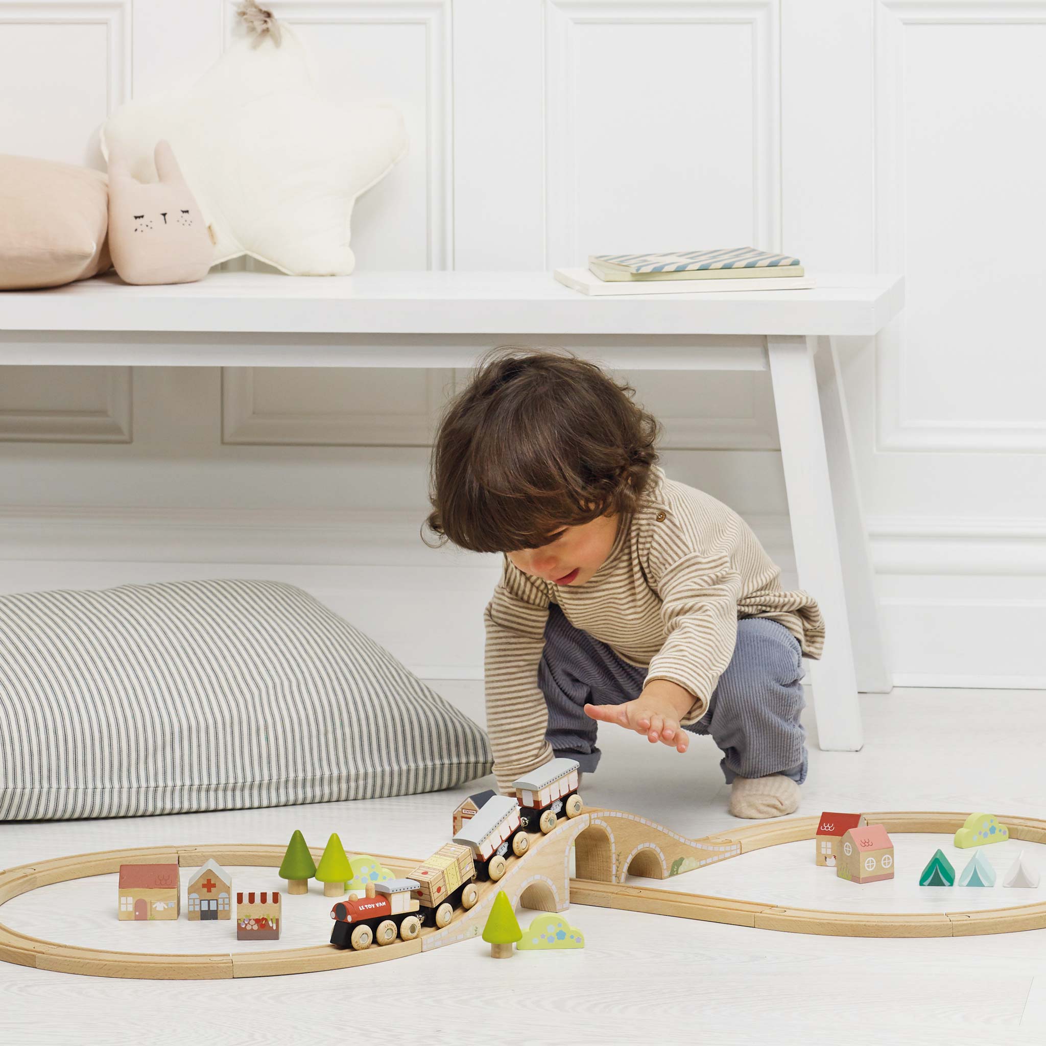 Child playing with a wooden train set on a white floor.