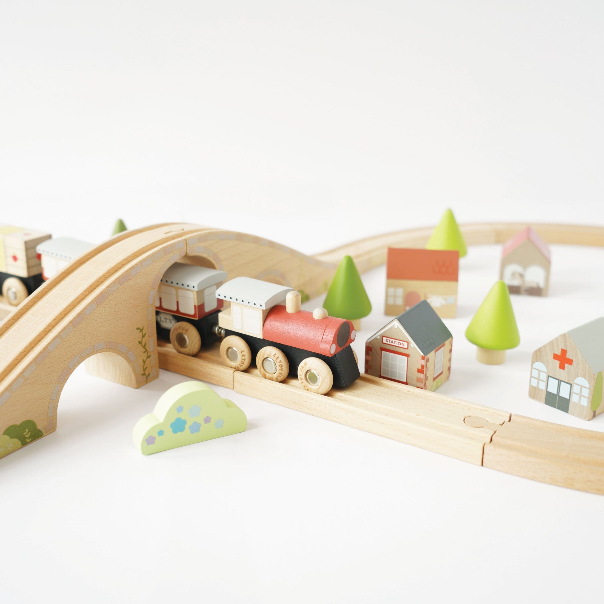 Wooden toy train set with tracks, bridge, and colorful buildings on a white background