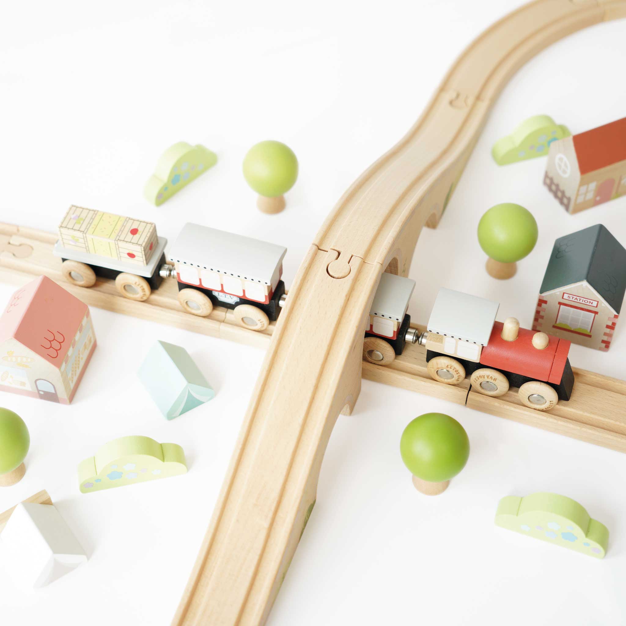 Wooden toy train set with tracks and small buildings on a white background