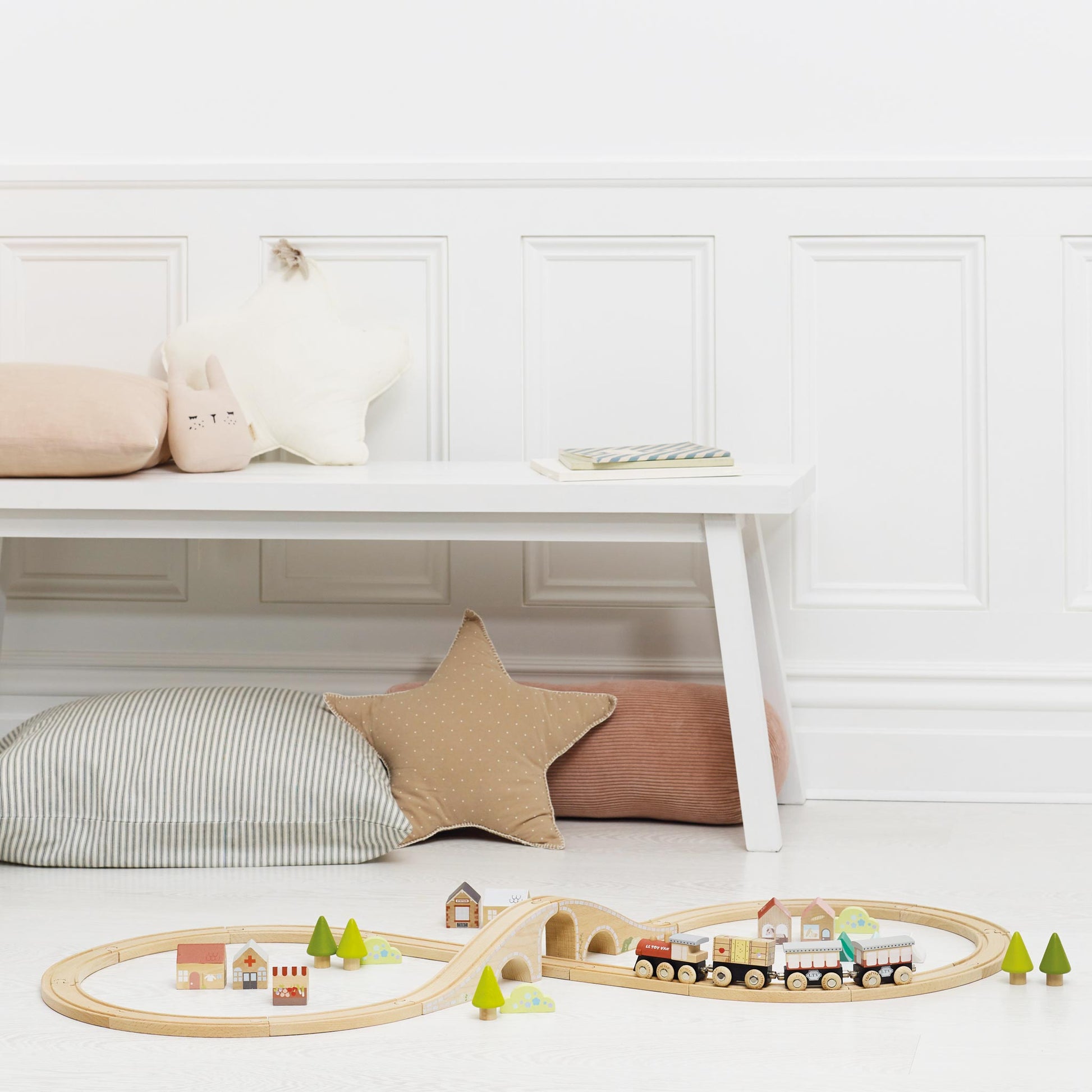 Wooden train set on a light wooden floor with star-shaped cushions on a white bench.