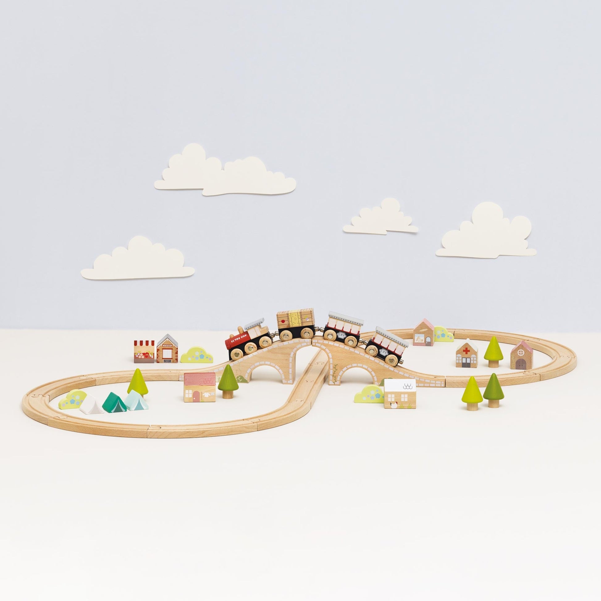 Wooden train set with tracks, trees, and houses on a light blue background