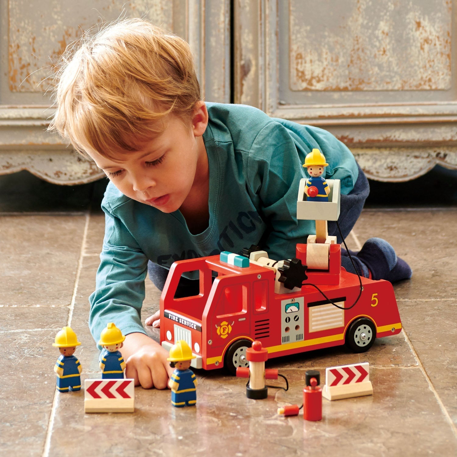 Child playing with a toy fire truck and figures on a wooden floor.