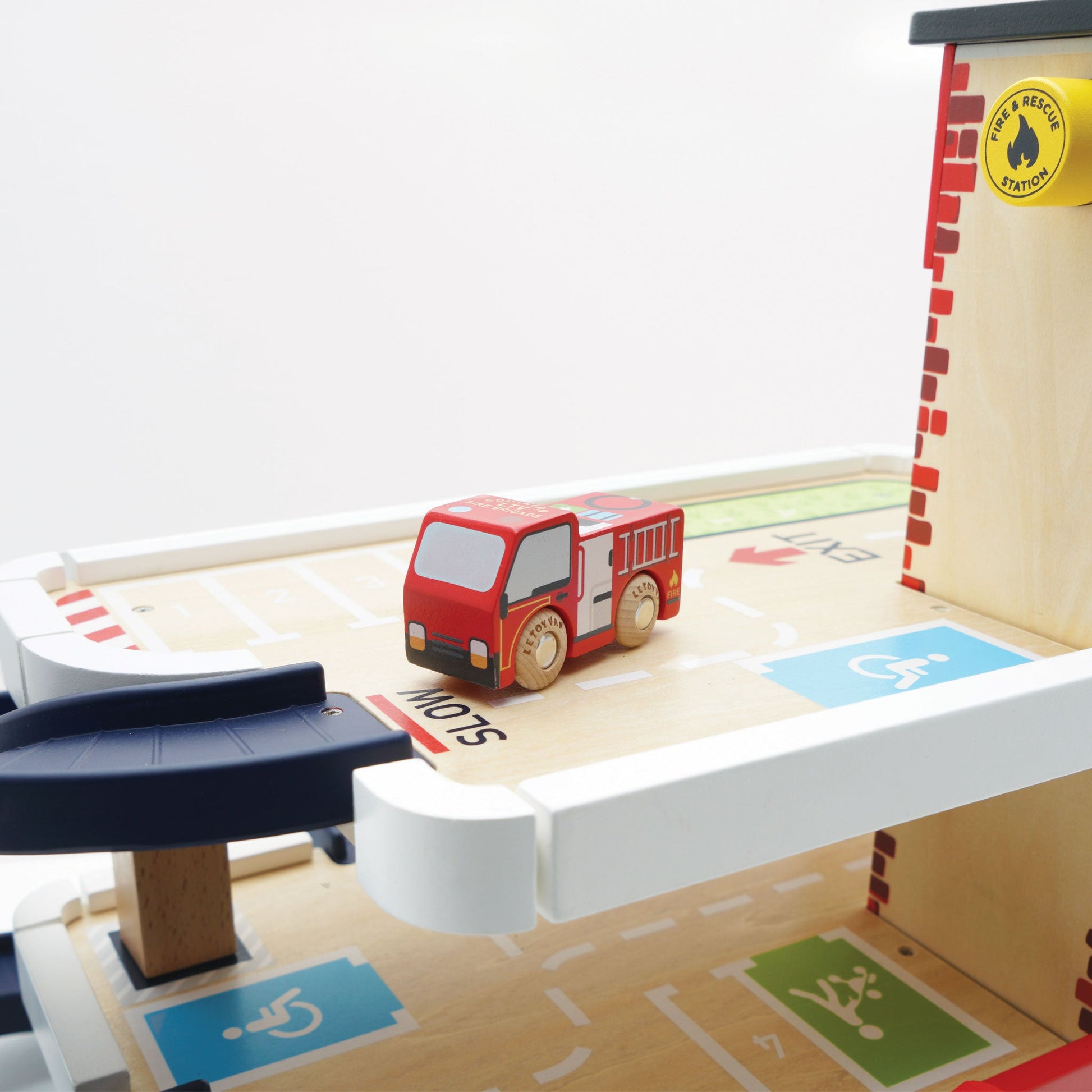 Red toy fire truck on a wooden playset with traffic signs and a fire station sign.