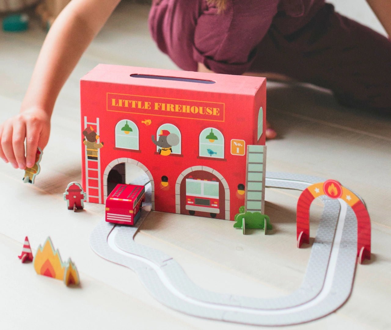 Children's toy set with a 'Little Firehouse' box, fire truck, and accessories on a light surface.
