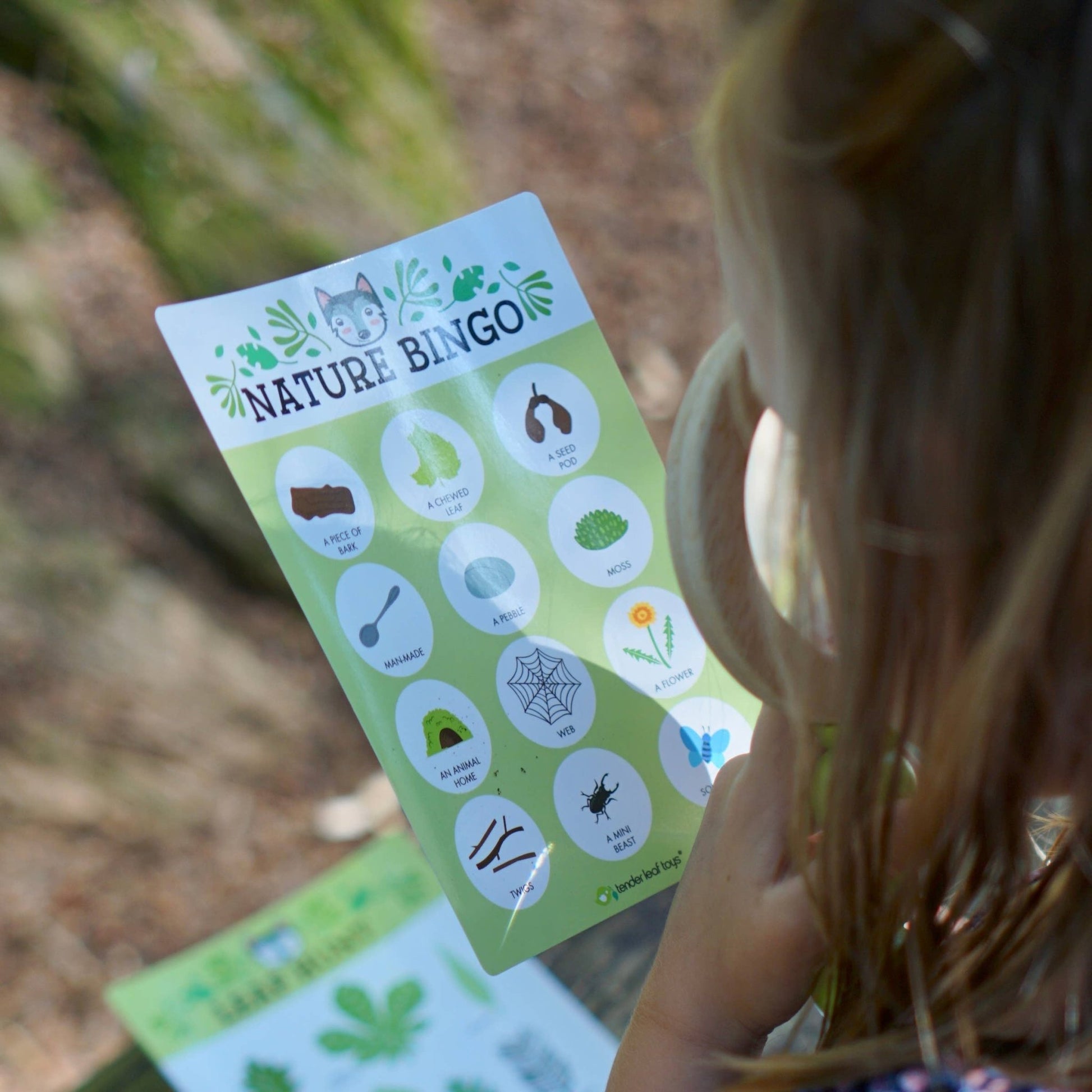 Child holding a nature bingo card with outdoor items on a wooden surface