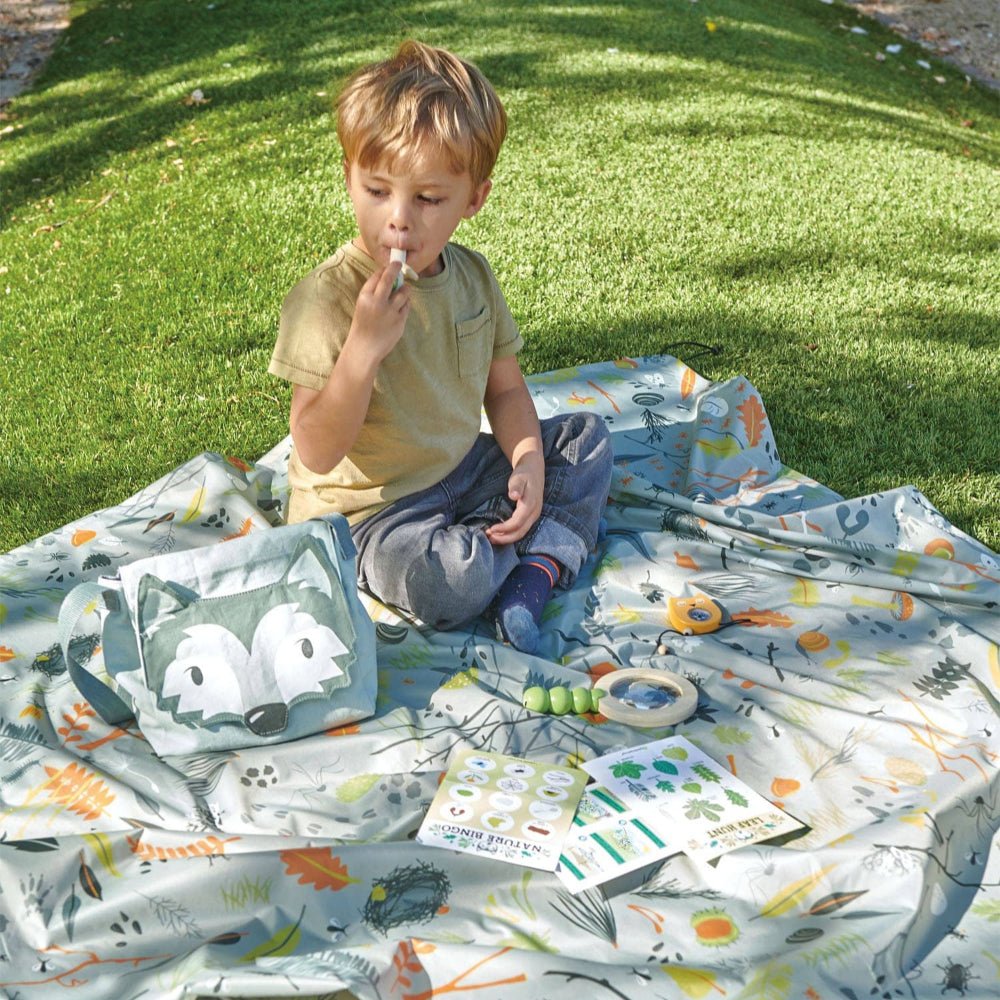 Child sitting on a colorful blanket with animal patterns in a grassy area