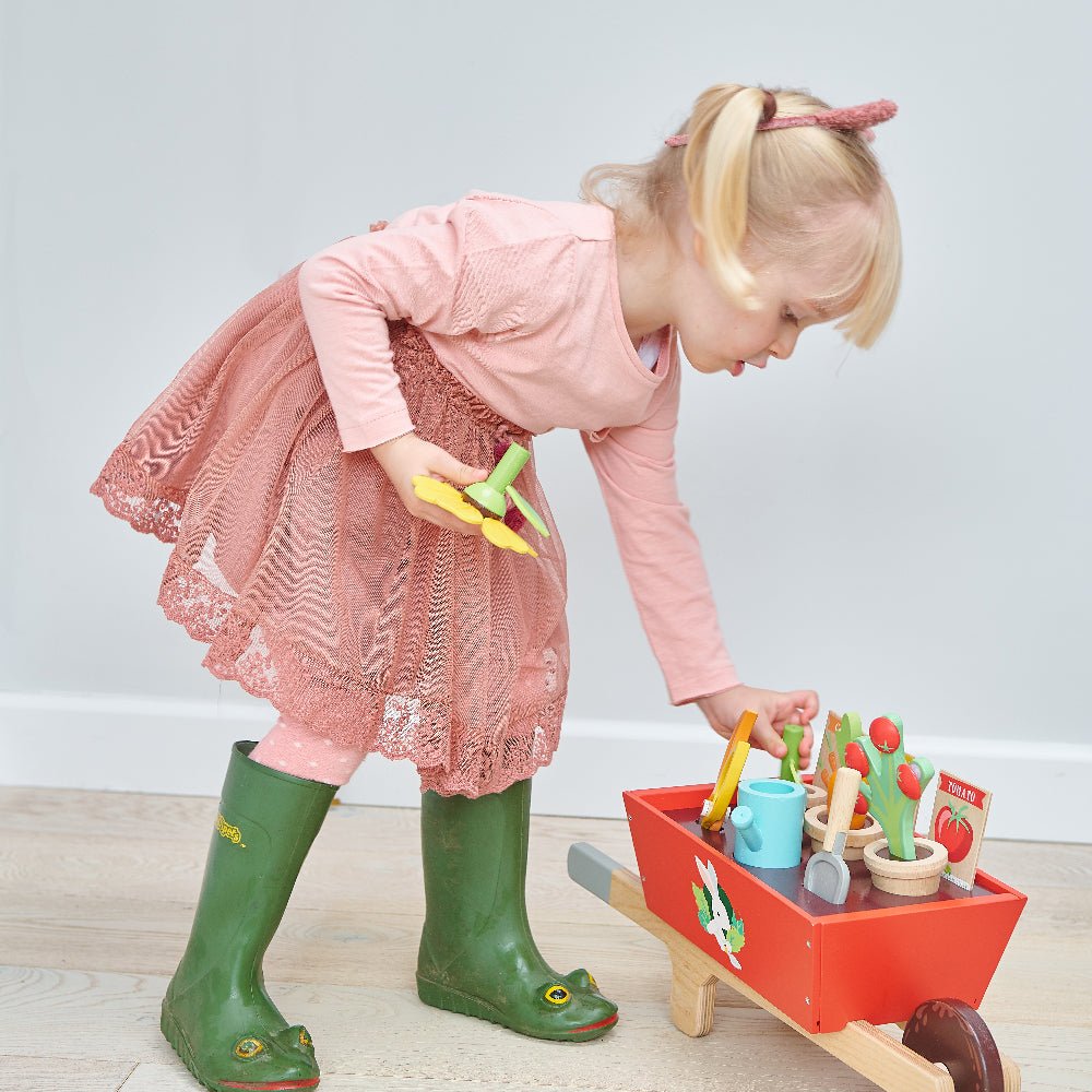 Child playing with a toy garden set on a light wooden floor.